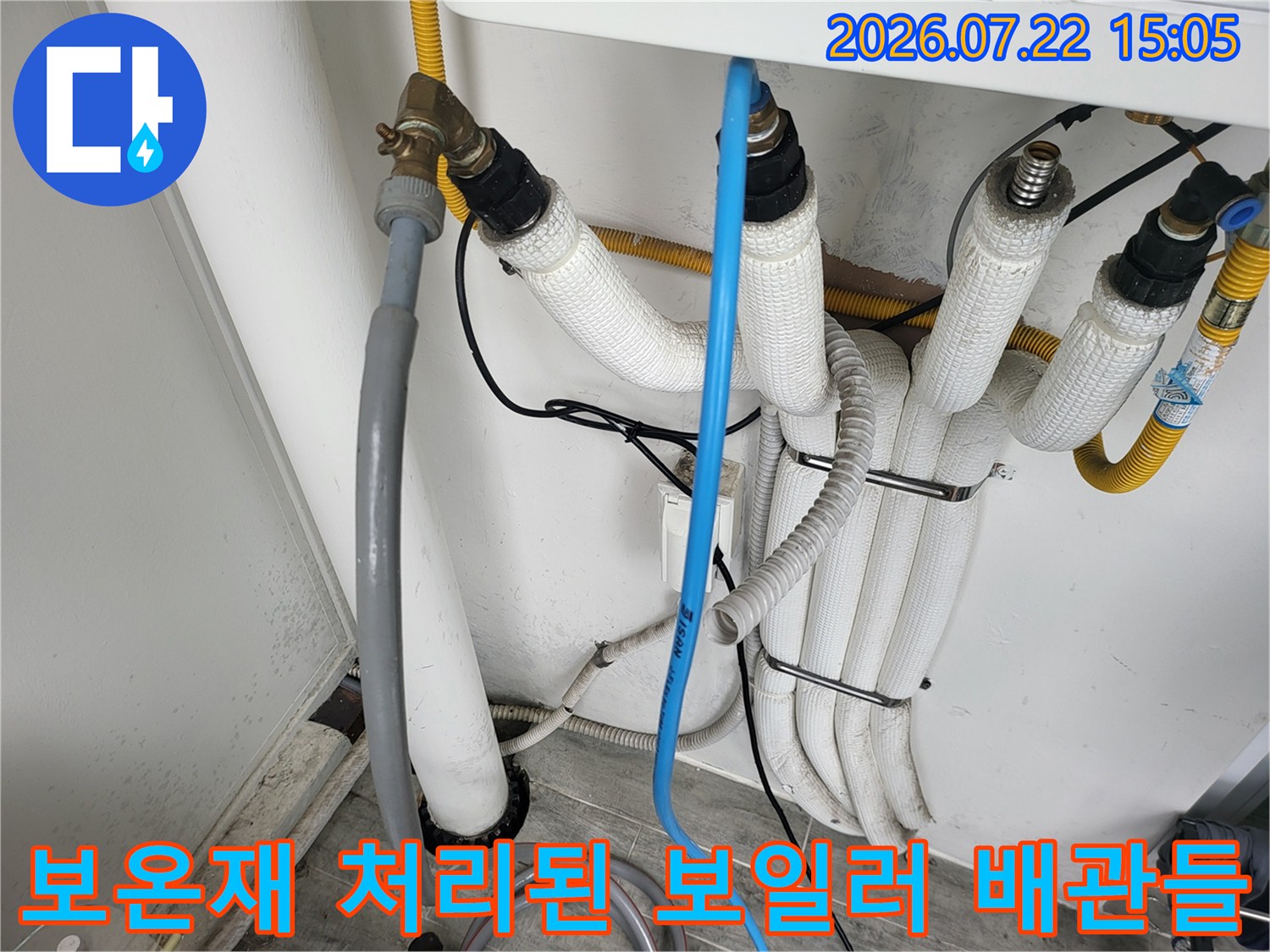여러 갈래로 나뉜 흰색 배관 보온재-금속 밸브와 파란색 호스가 연결된 모습