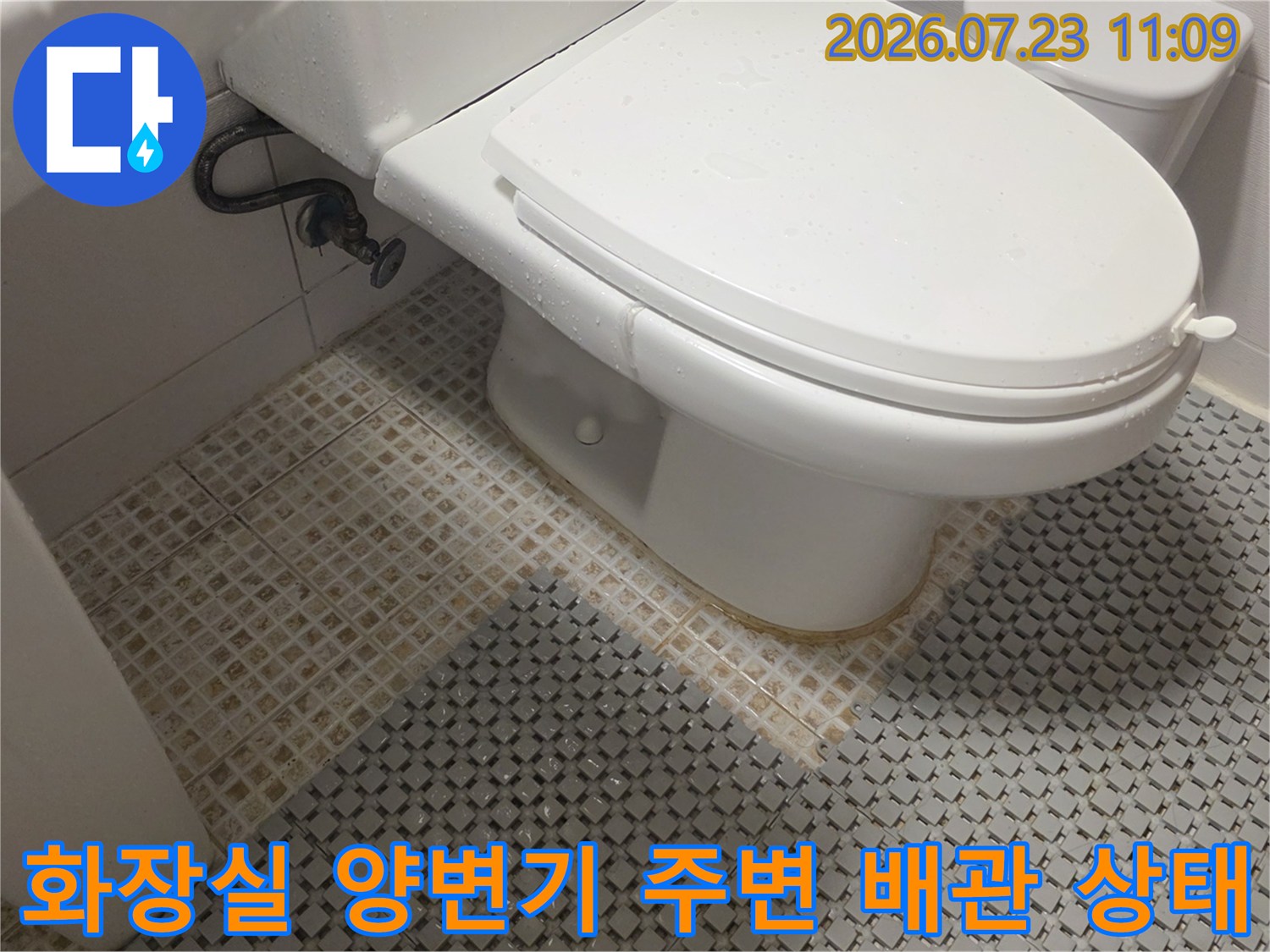흰색 양변기와 그 옆으로 연결된 검은색 고무 호스 배관 모습