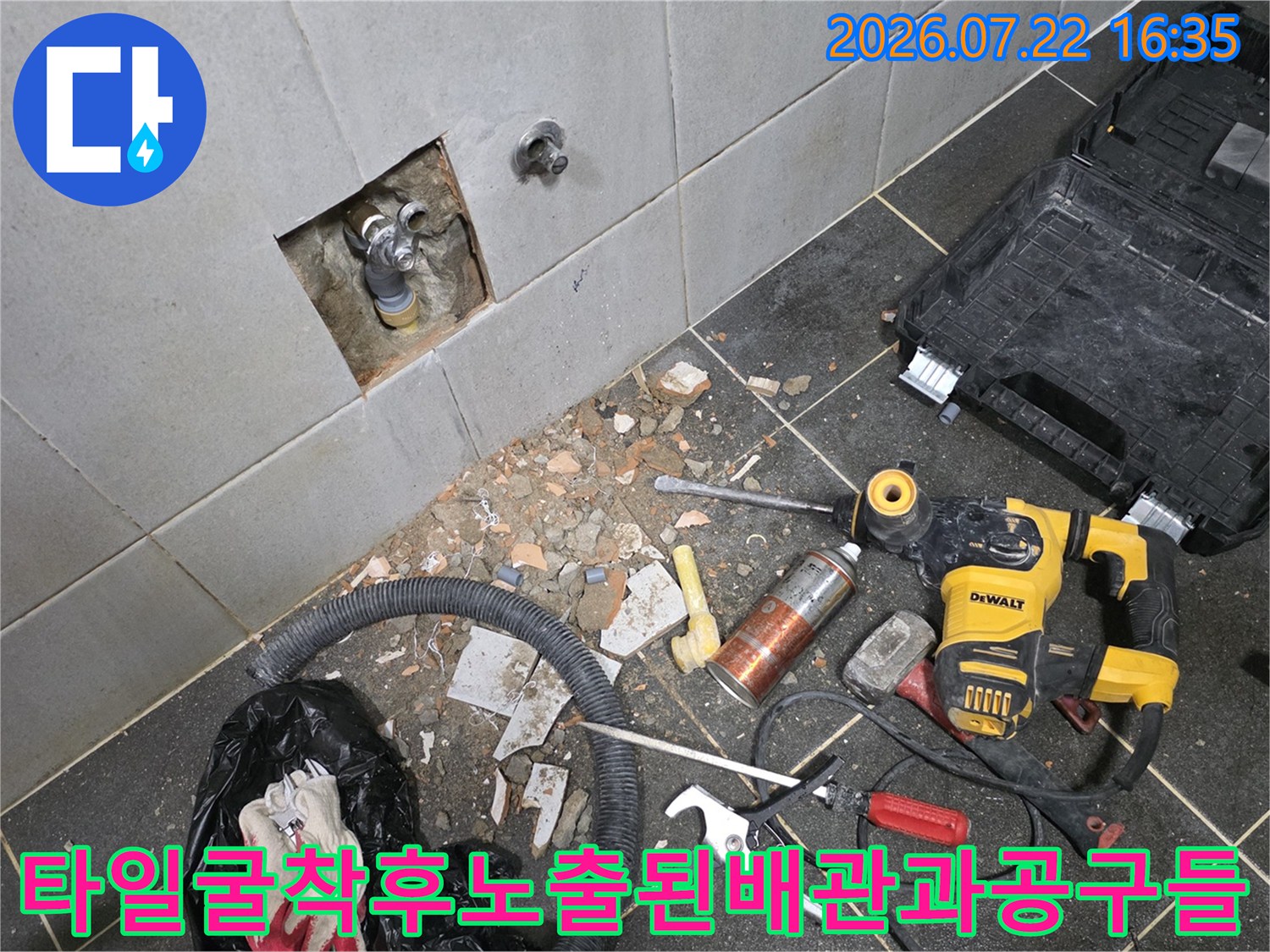 세탁실 타일 벽면을 굴착하여 매립된 수도 배관이 드러나 있고 주변에 전동드릴과 플라이어 등 공구가 놓인 모습