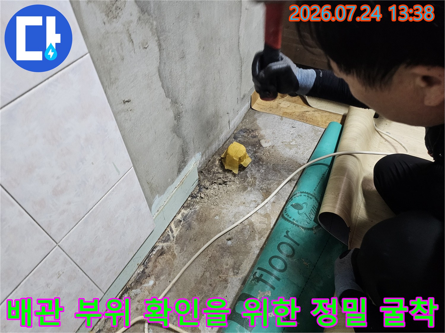 바닥에 녹색 보호 매트를 깔고 장비를 사용하여 누수 지점을 파내고 있는 현장 사진