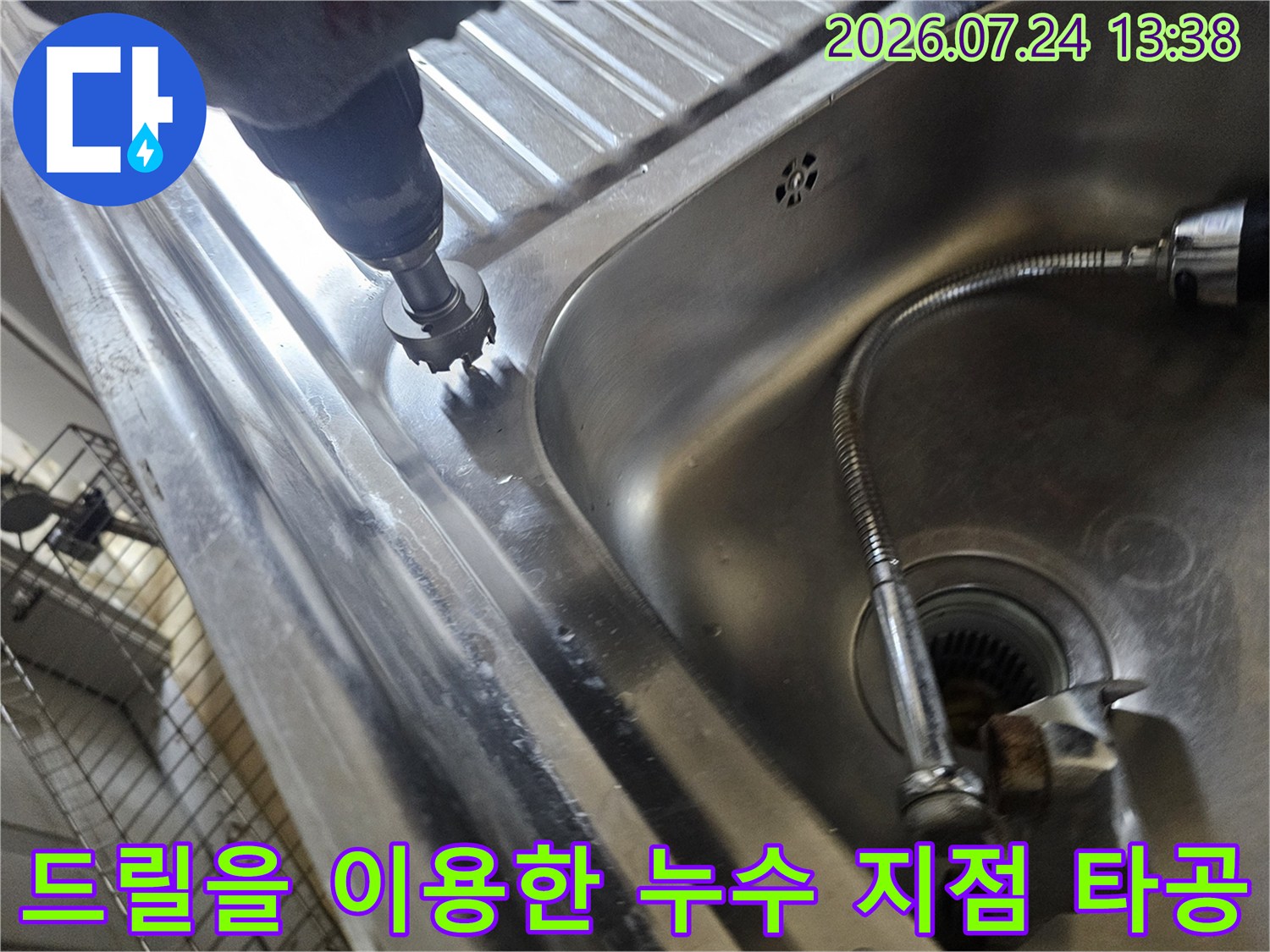스테인리스 소재의 싱크대 하부 영역에서 전동 드릴로 구멍을 뚫어 배관을 확인하는 사진