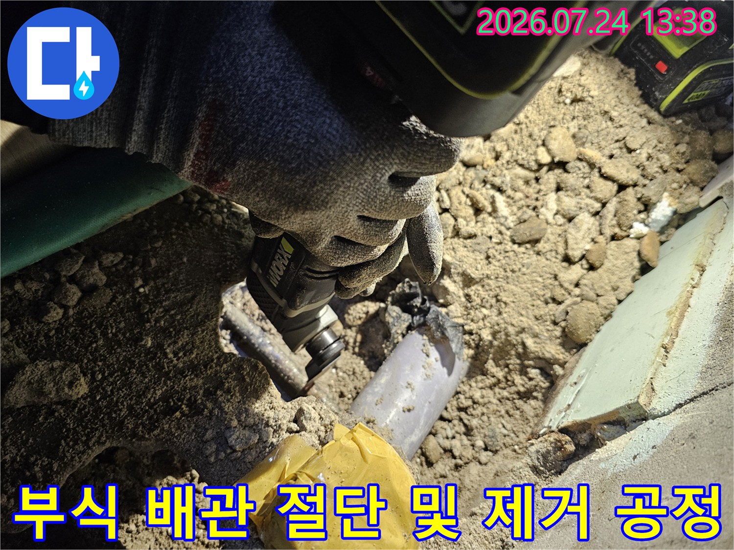 전동 공구를 사용하여 바닥 매립된 낡은 금속 배관을 잘라내고 있는 작업자의 모습