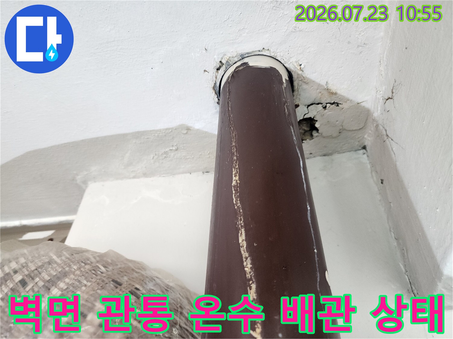 흰색 벽체를 통과하는 갈색 온수 배관-주변 시멘트 마감재의 균열과 틈새 모습
