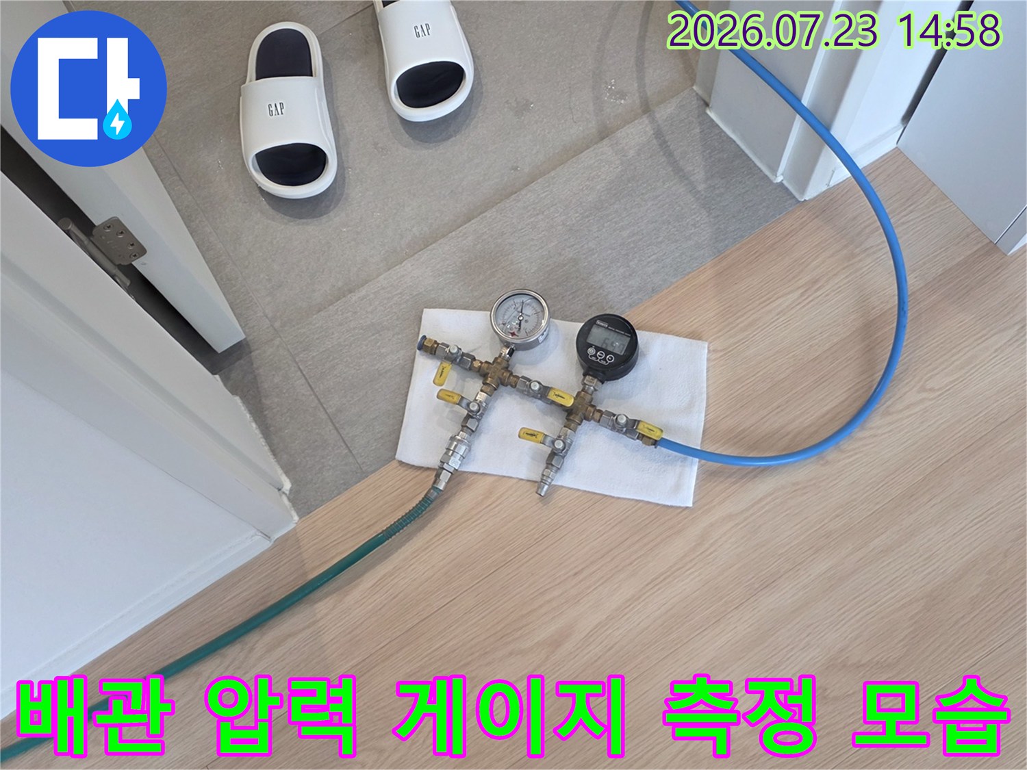 바닥에 놓인 흰 수건 위에 공압 테스트용 압력 게이지와 파란색 호스가 연결된 장비-사진