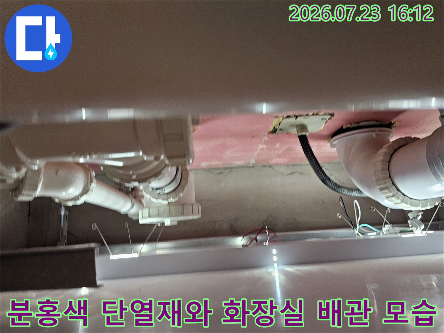 화장실 천장의 분홍색 단열재 아래로 설치된 흰색 하수 배관-곡선 연결 부위