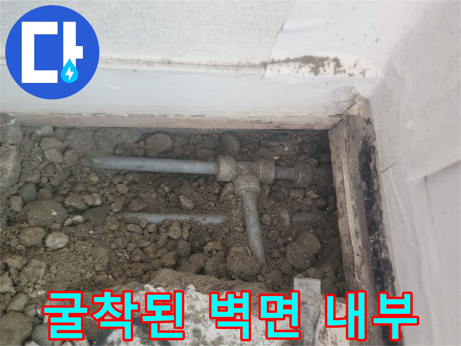 벽면 하단 흙과 자갈 사이로 노출된 수도 배관의 상태