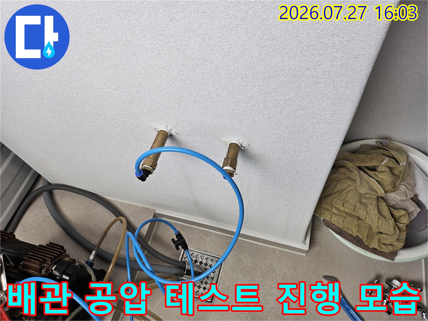 흰색 벽면에 설치된 배관 연결부에 파란색 호스를 연결하여 공압 테스트를 진행하는 모습