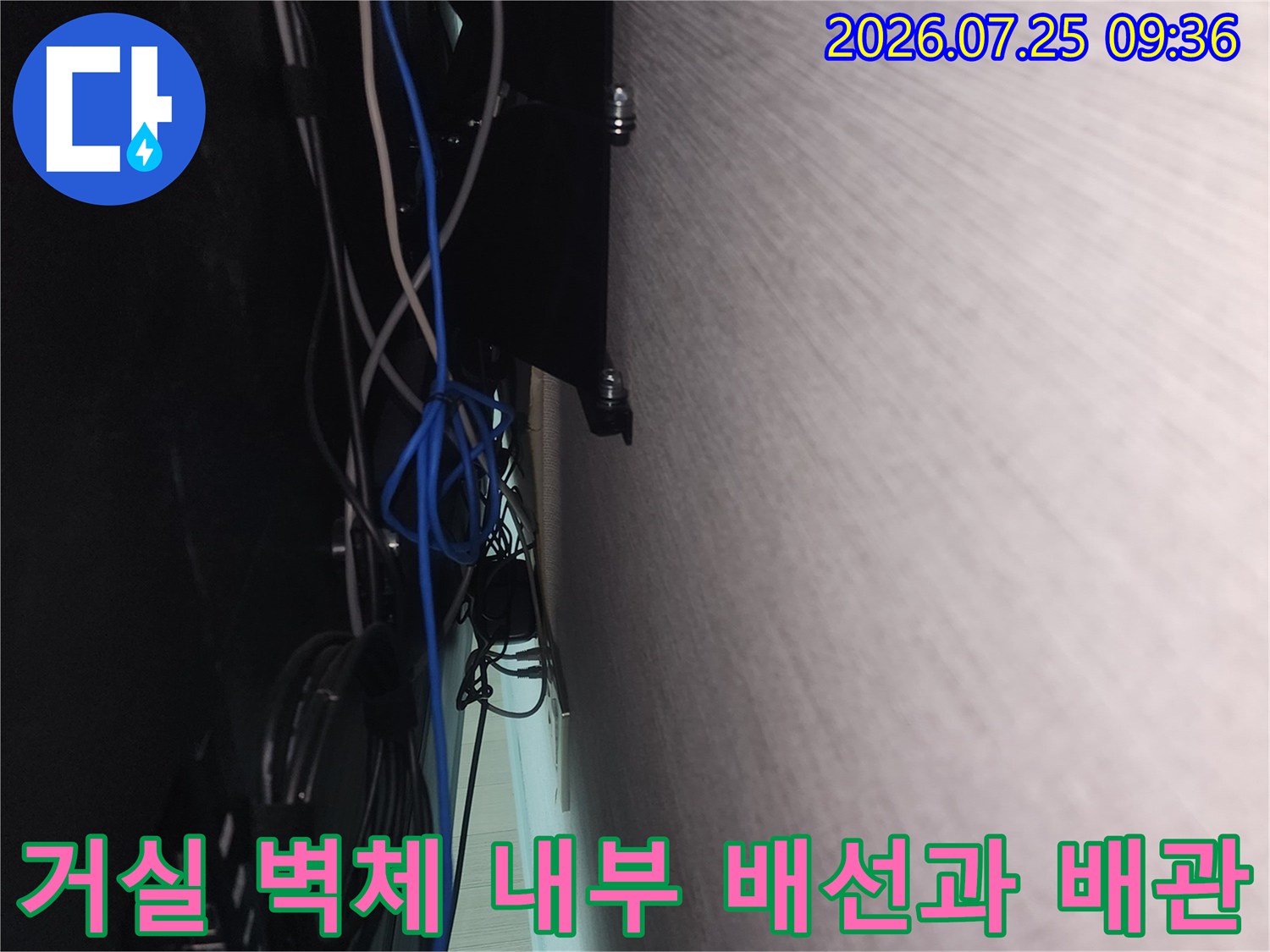 복잡하게 얽힌 전선들과 연결된 배관이 노출된 거실 벽면 점검 장면