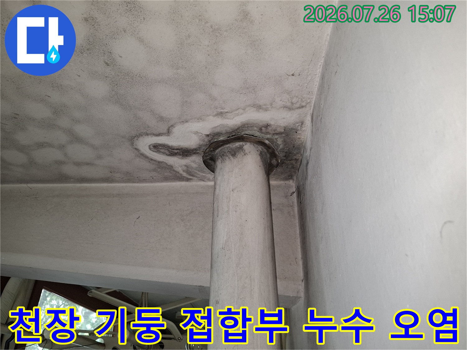 흰색 천장 마감재와 원형 기둥 사이 틈새로 번진 어두운 색상의 누수 오염-근접 사진