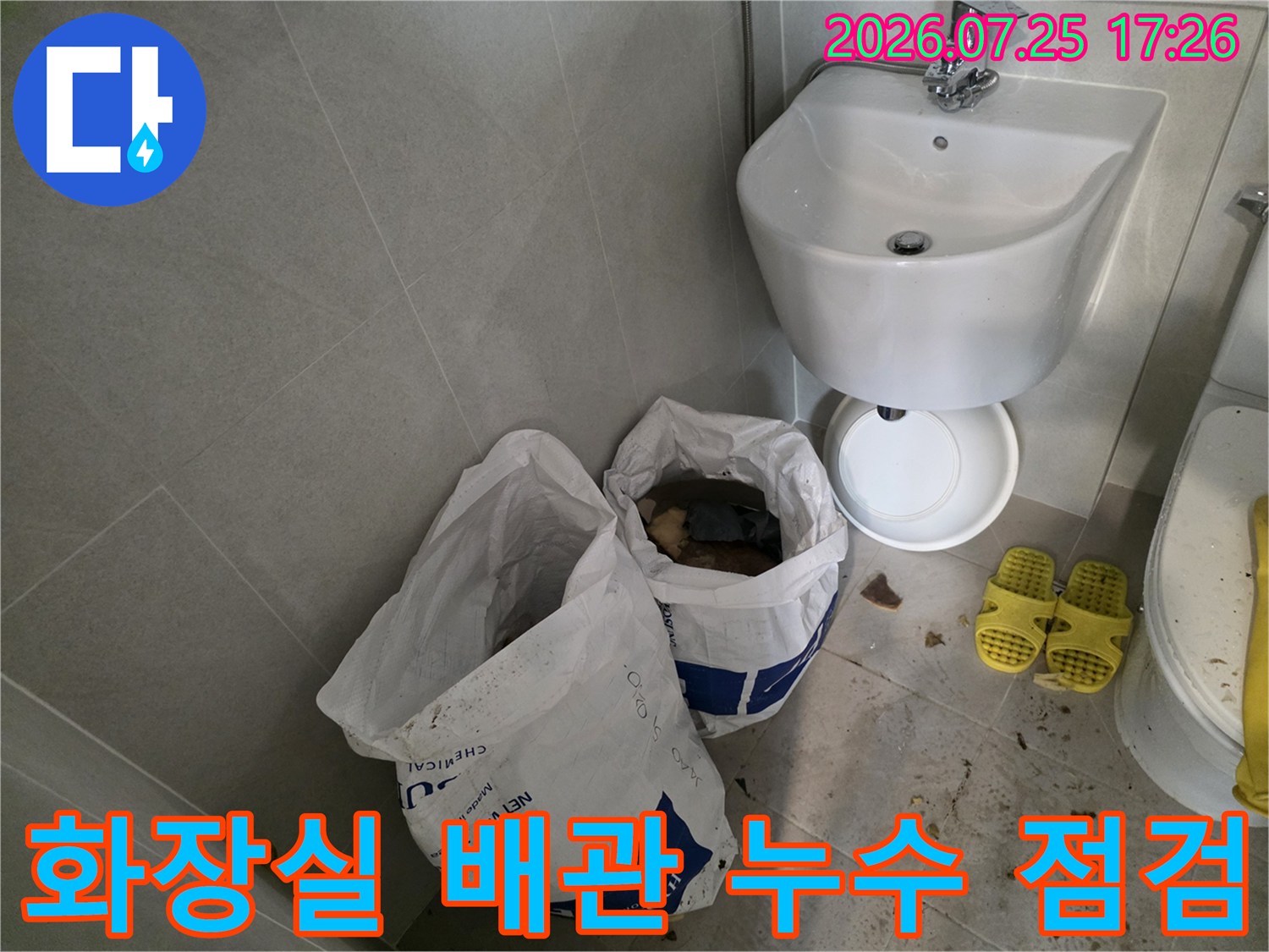 화장실 세면대 아래 공간에 배치된 대형 폐기물 수거용 포대와 노출된 배관 시설