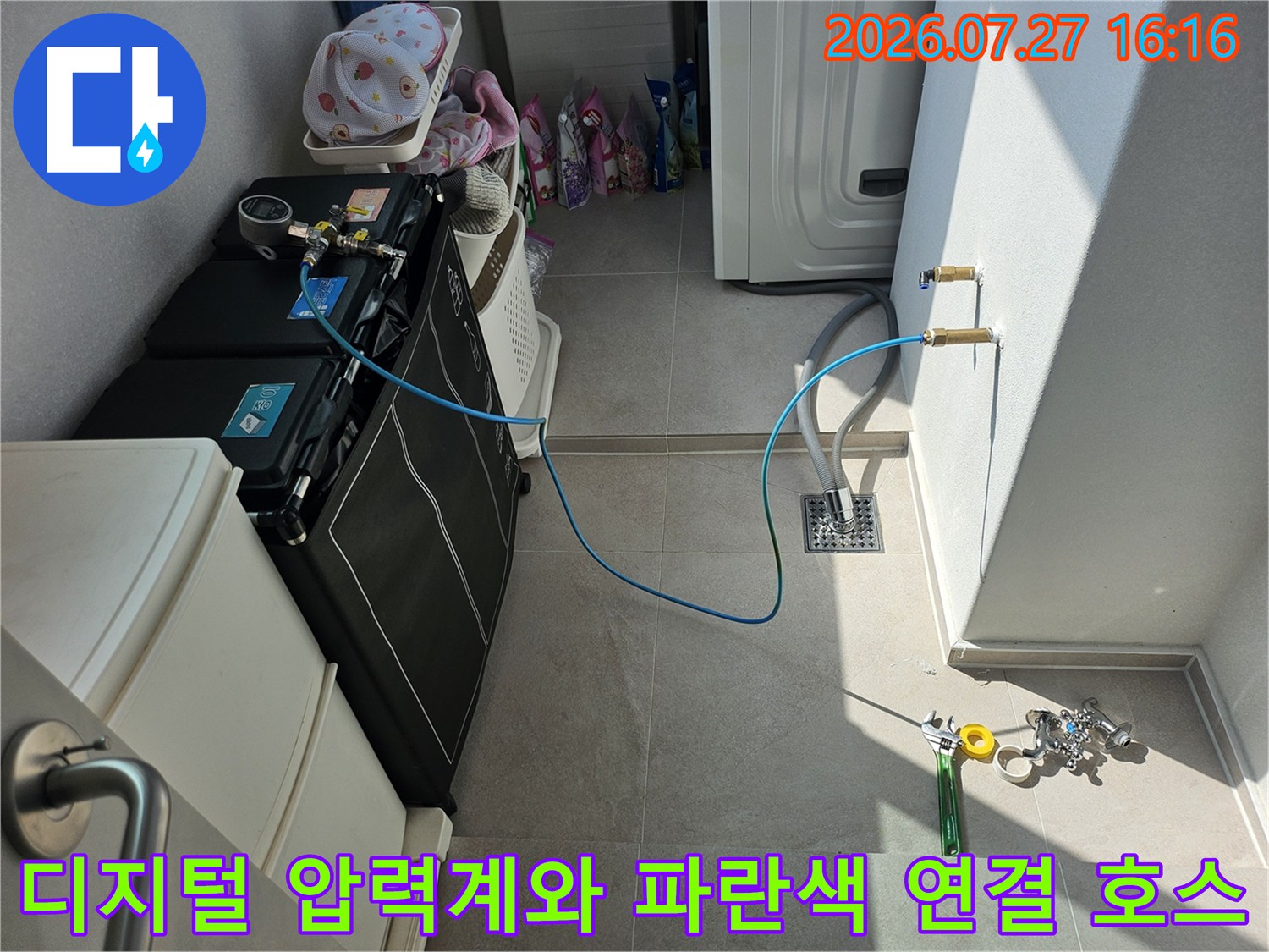 바닥의 타일 위로 파란색 호스가 길게 이어져 벽면 밸브와 누수 탐지 장비가 연결된 상태