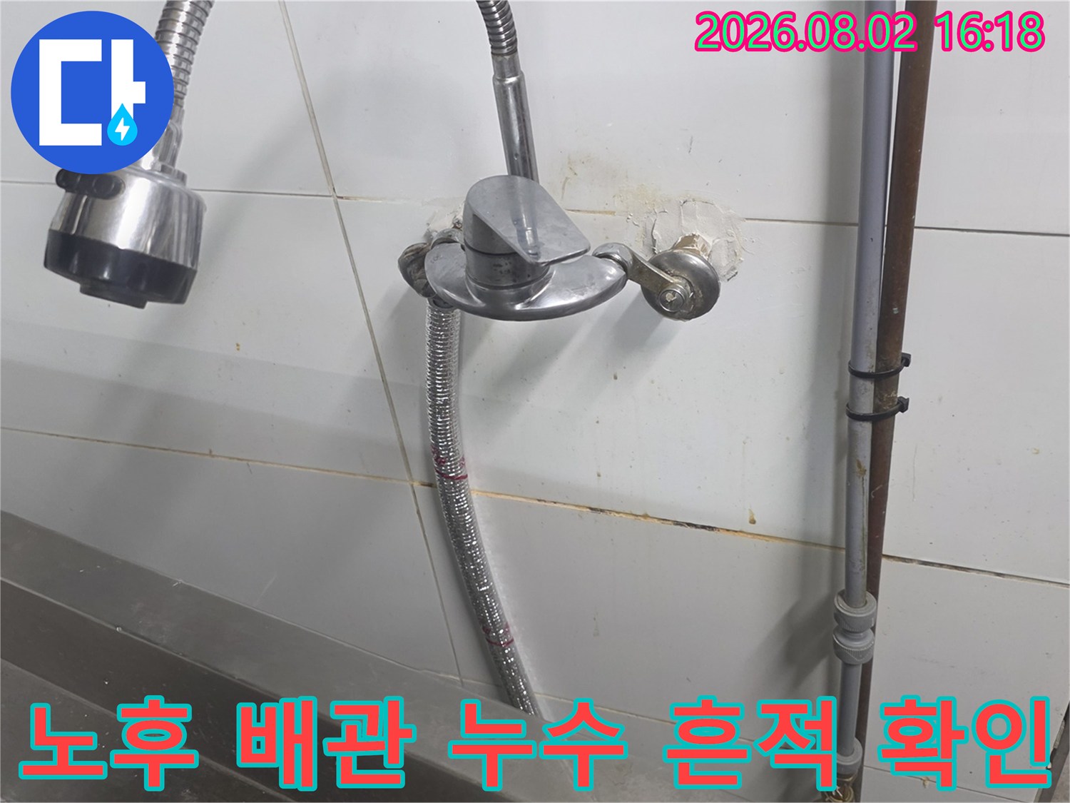 벽면 타일 주변에 노출된 주방 급수 배관과 누수 오염 부위
