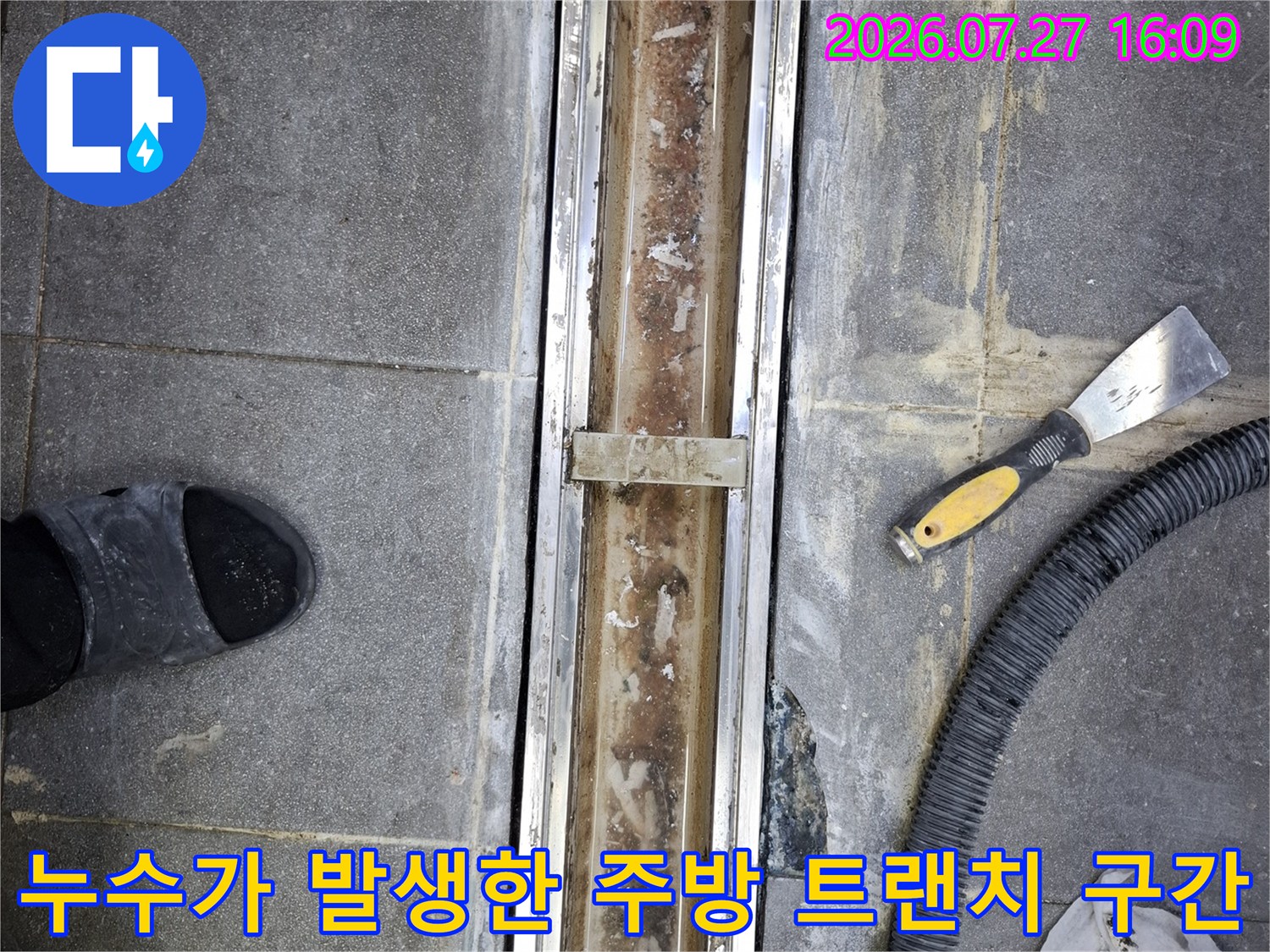 회색 타일 바닥에 설치된 스테인리스 배수 트랜치의 내부-작업 도구가 주변에 흩어져 있는 현장 사진