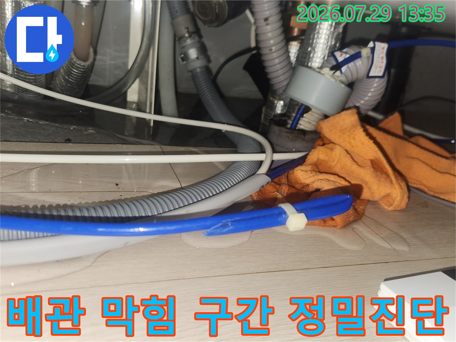작업용 장갑과 배수 호스가 배치된 싱크대 하부 작업 공간