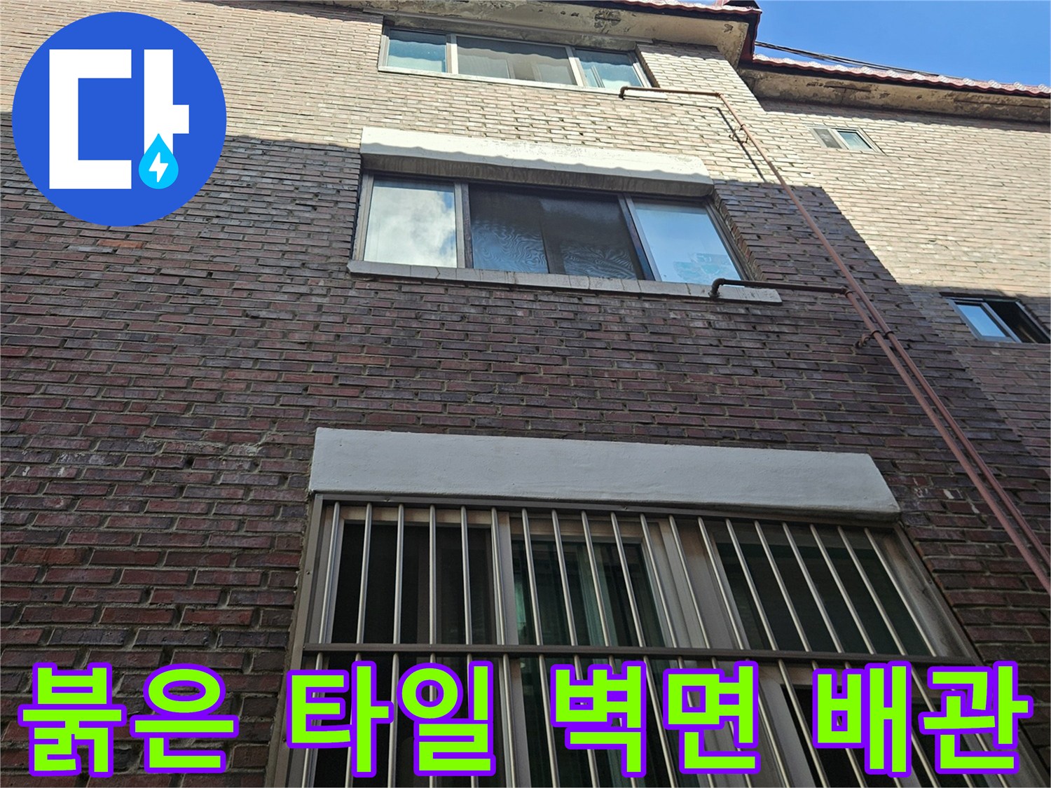 적갈색 타일로 된 건물 외벽과 수직으로 내려오는 배관입니다.