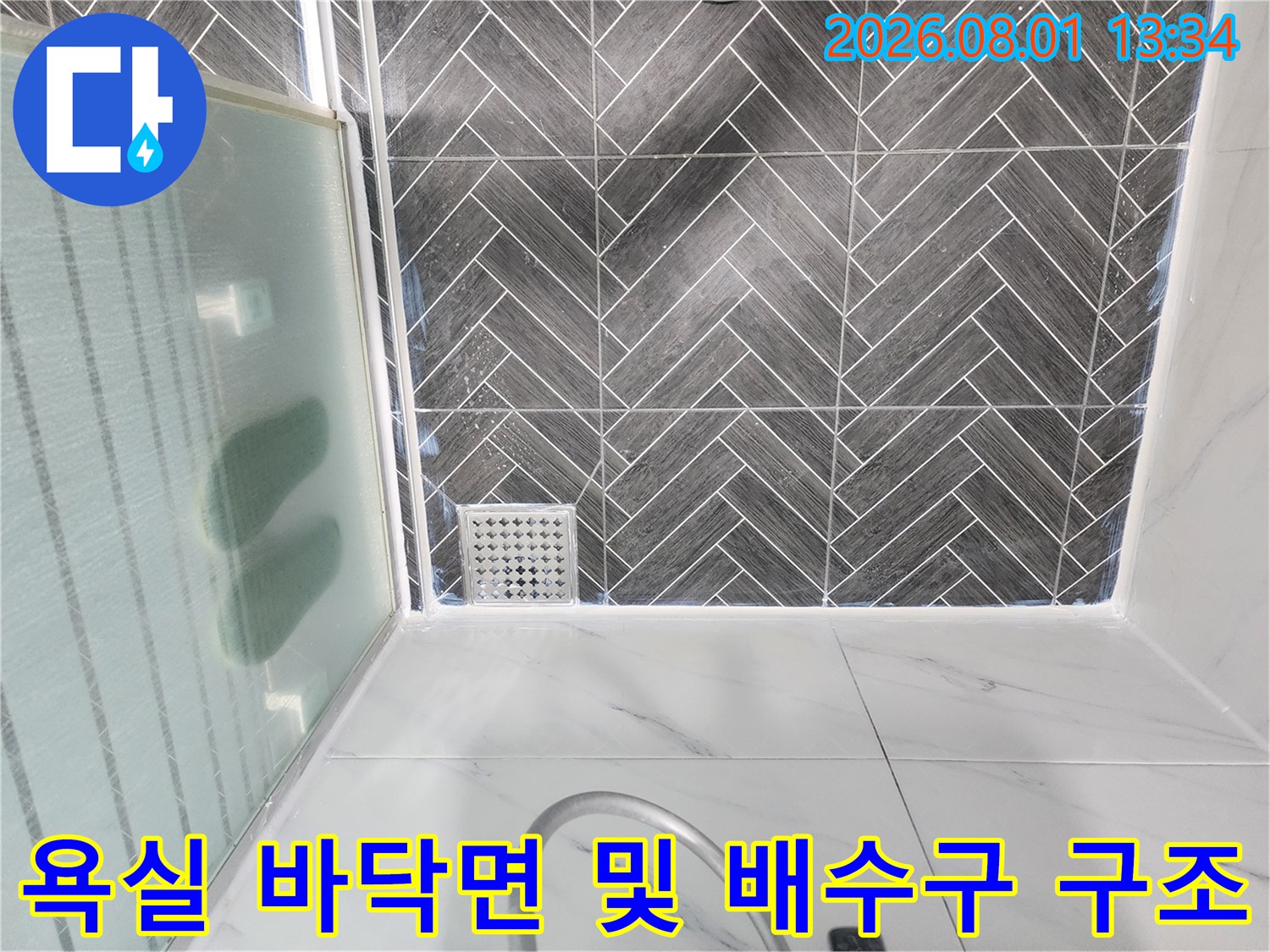 회색 계열의 헤링범 타일과 금속 소재 느낌의 사각형 배수구