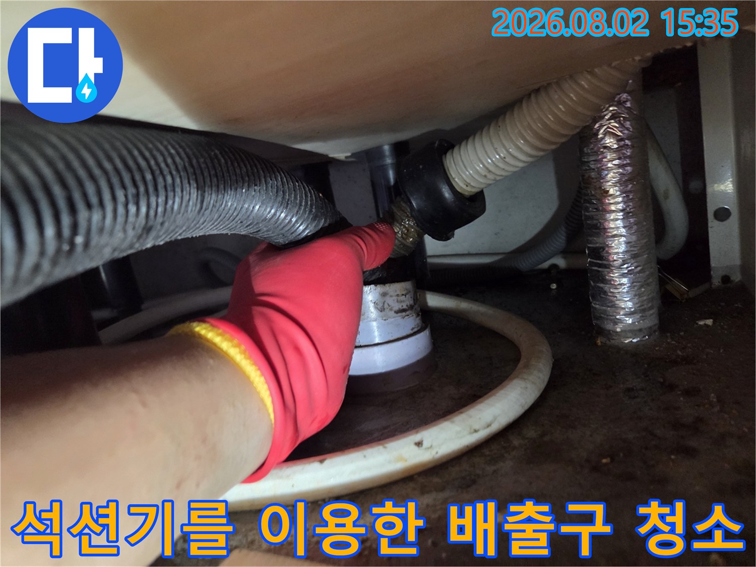 싱크대 하부의 배수관 입구에 석션 호스를 연결하여 내부 이물질을 제거하는 장면