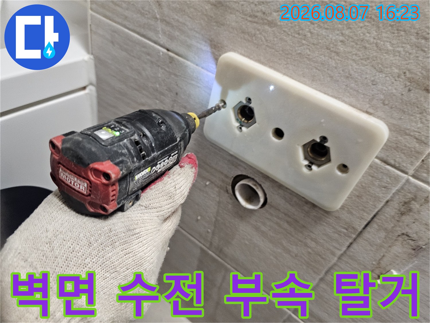 타일 벽면에 노출된 급수 배관 연결 부위를 전동 공구로 작업하는 장면입니다.