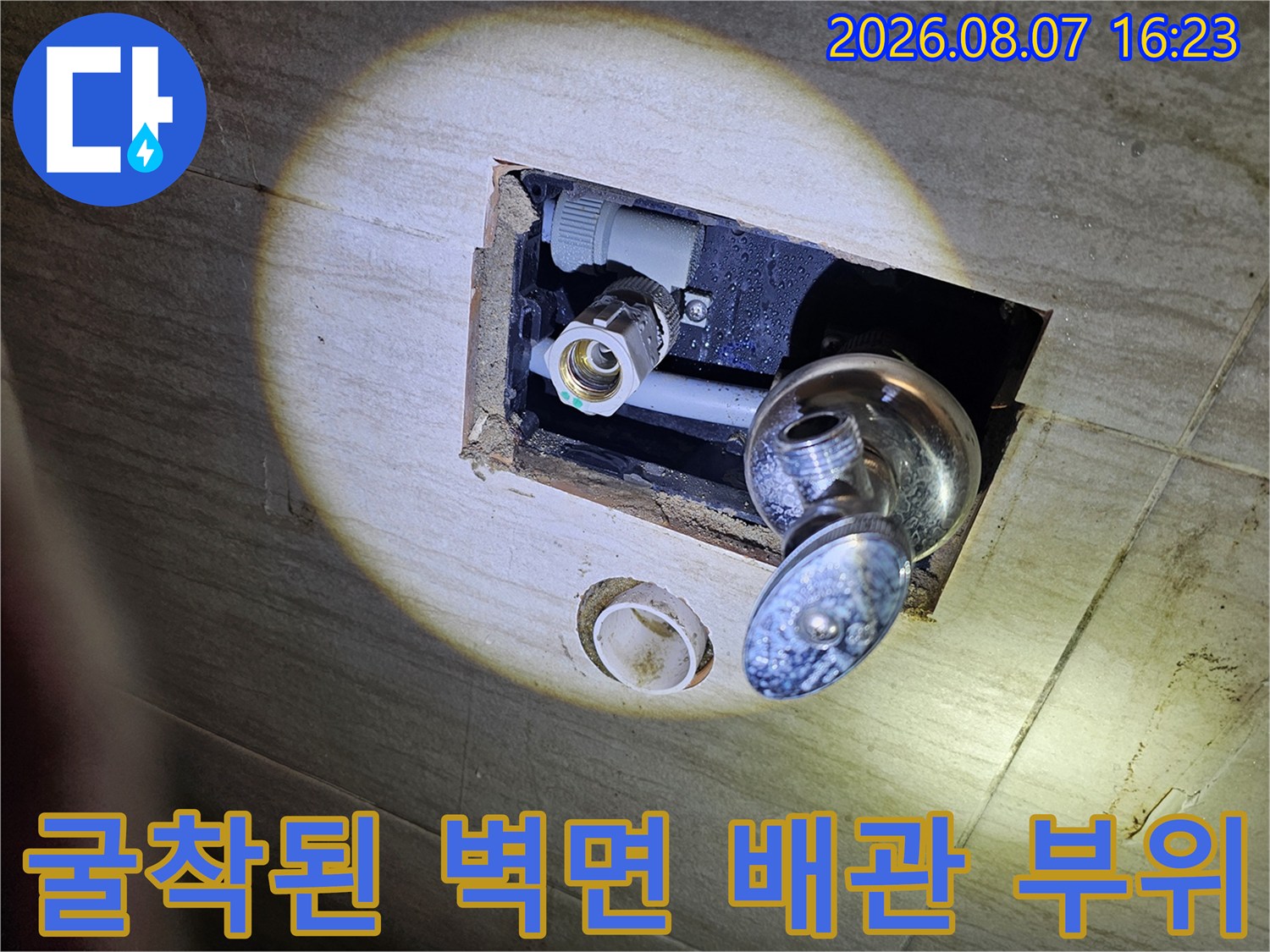 타일 틈 사이로 노출된 수도 수전과 연결된 회색 매립 배관의 균열 확인 작업