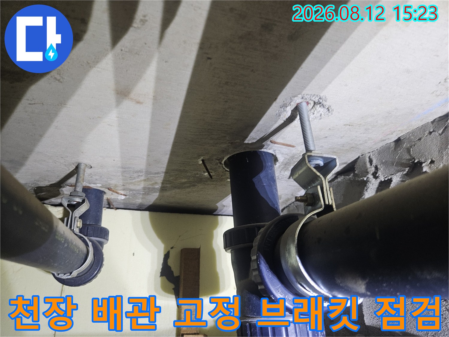 검은색 PVC 배관을 천장에 고정시키고 있는 은색 금속제 지지대와 볼트 체결 부분