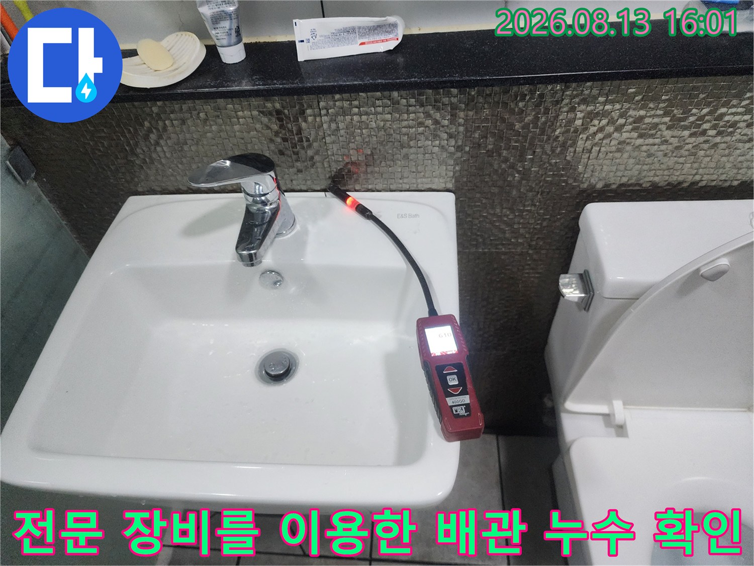 붉은색 가스 탐지기가 세면대 뒤쪽 벽체 배관 부근에서 반응을 나타내며 작동하고 있습니다.