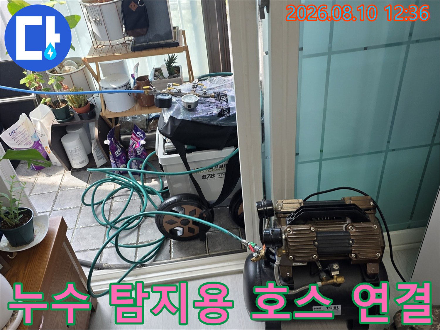 베란다 바닥 배관에 연결된 파란색 에어 호스와 압력 테스트 장비