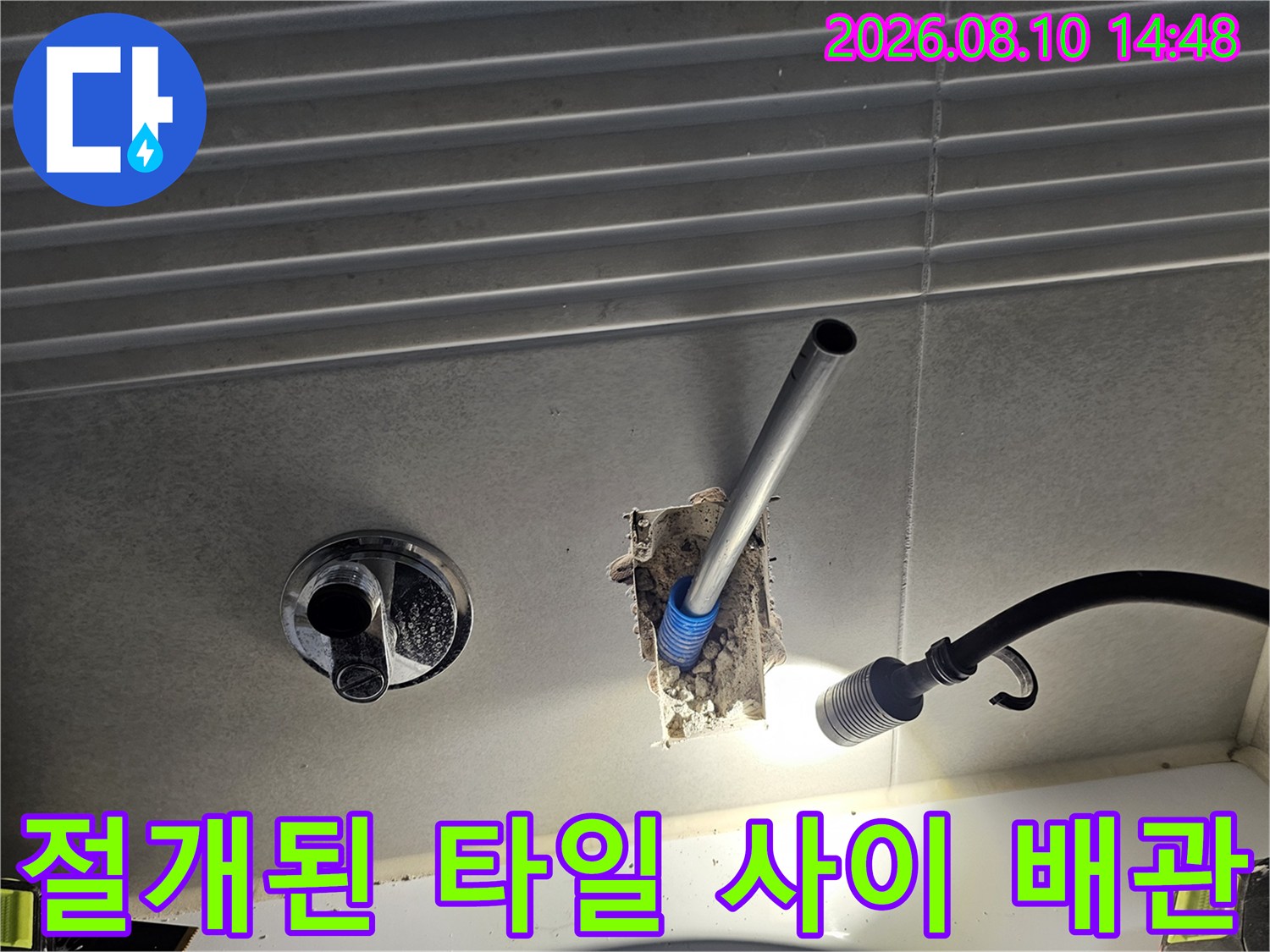 타일을 절개하여 노출시킨 벽면 내부의 은색 배관과 수전 연결 부위 점검 상황입니다.