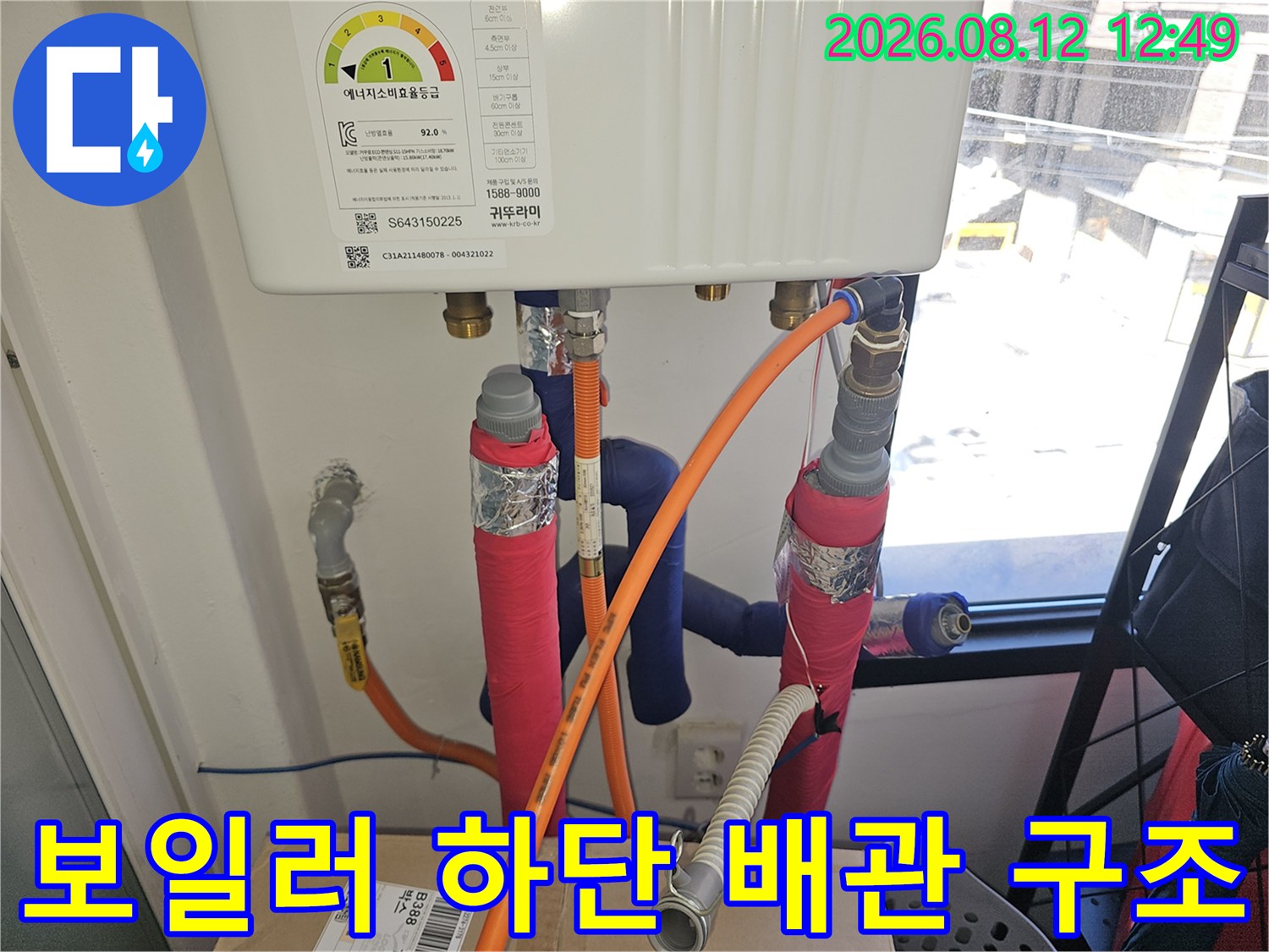 보일러 밑으로 연결된 주황색 호스와 분홍색 보온재 배관