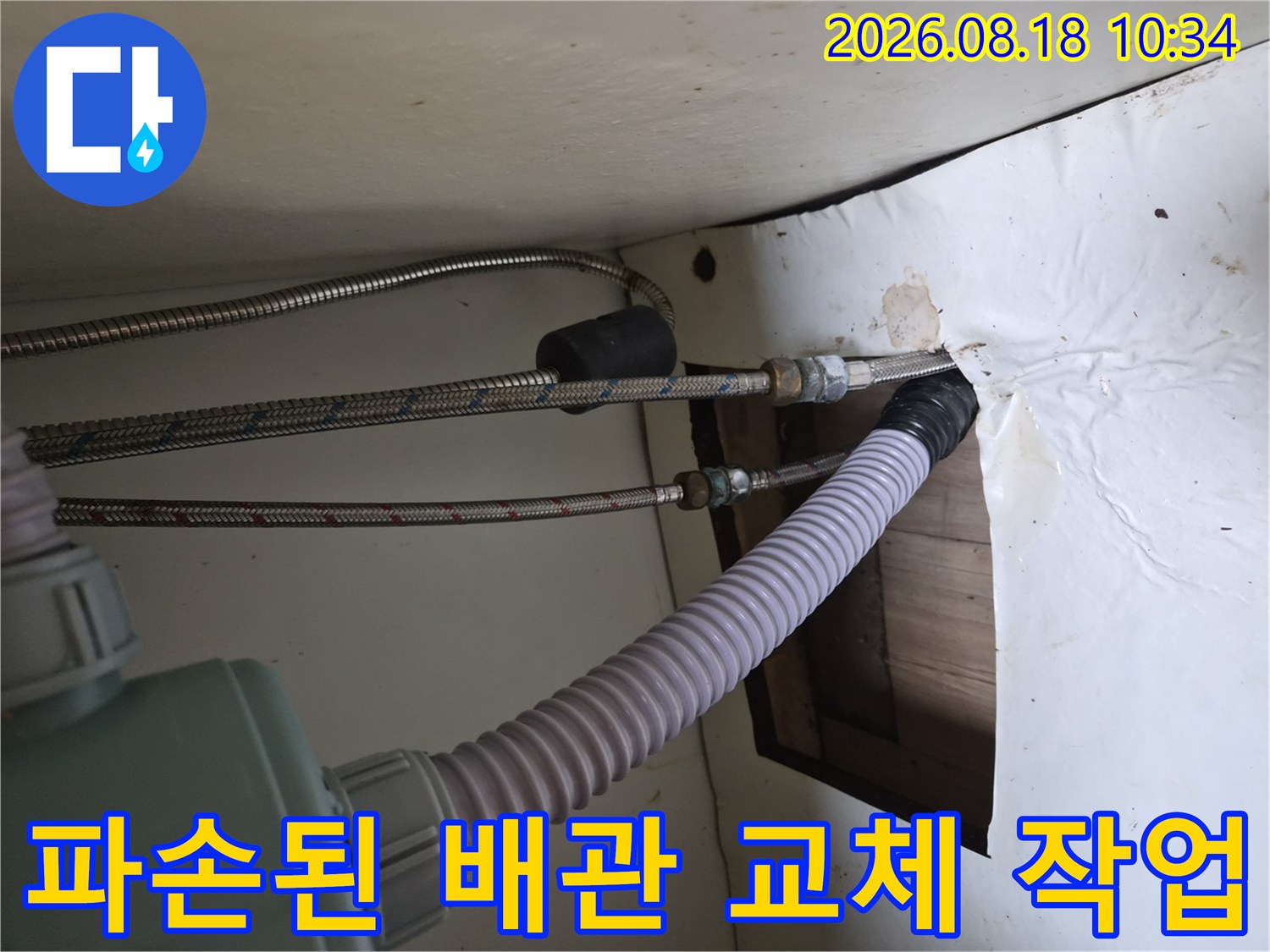 싱크대 하단부-금속 고압 호스와 흰색 주름관이 연결되어 있는 배관 구조입니다.