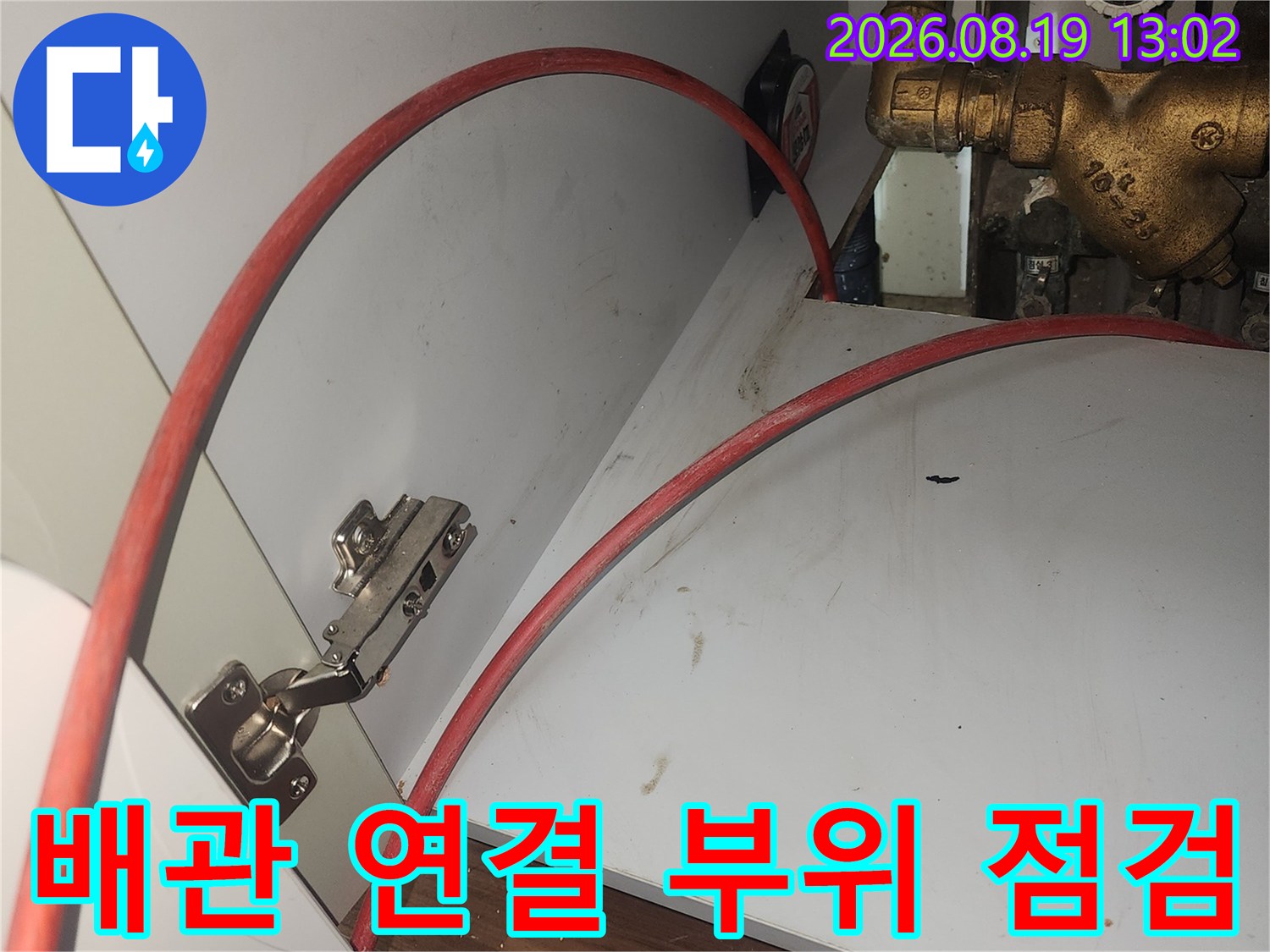 금속 밸브와 붉은색 호스가 연결된 싱크대 하부 배관 사진
