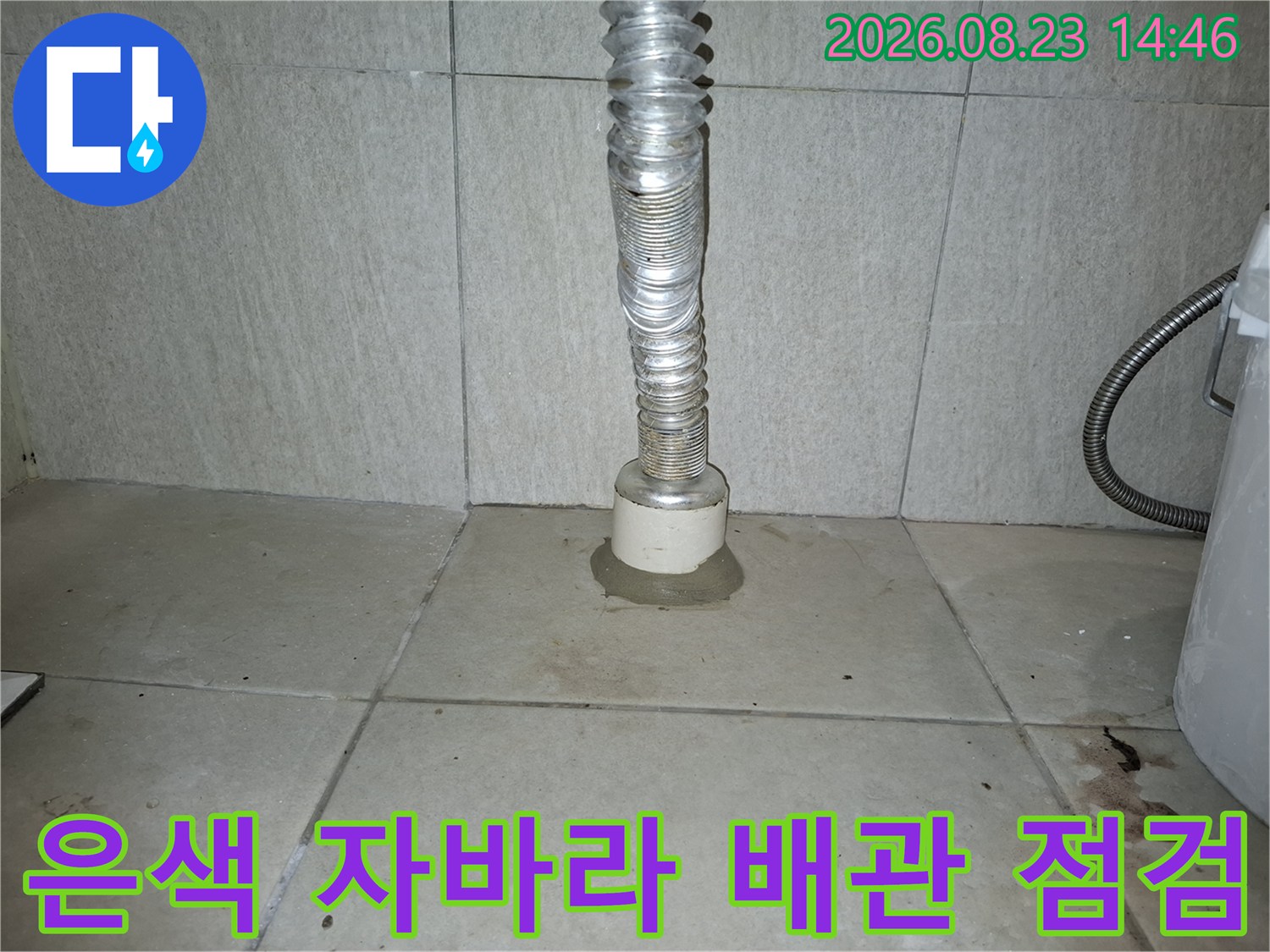 세탁실 바닥의 은색 주름관과 배수구 연결 부위 상세 사진입니다.
