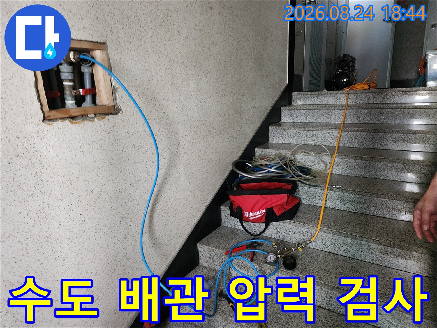 벽면에 노출된 흰색 배관과 연결된 파란색 테스트용 호스입니다.