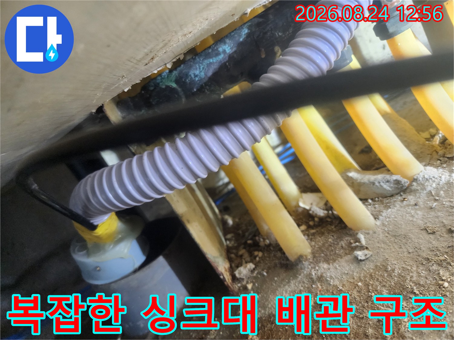 노란색 배수관과 흰색 호스가 연결된 싱크대 하부 배관 모습