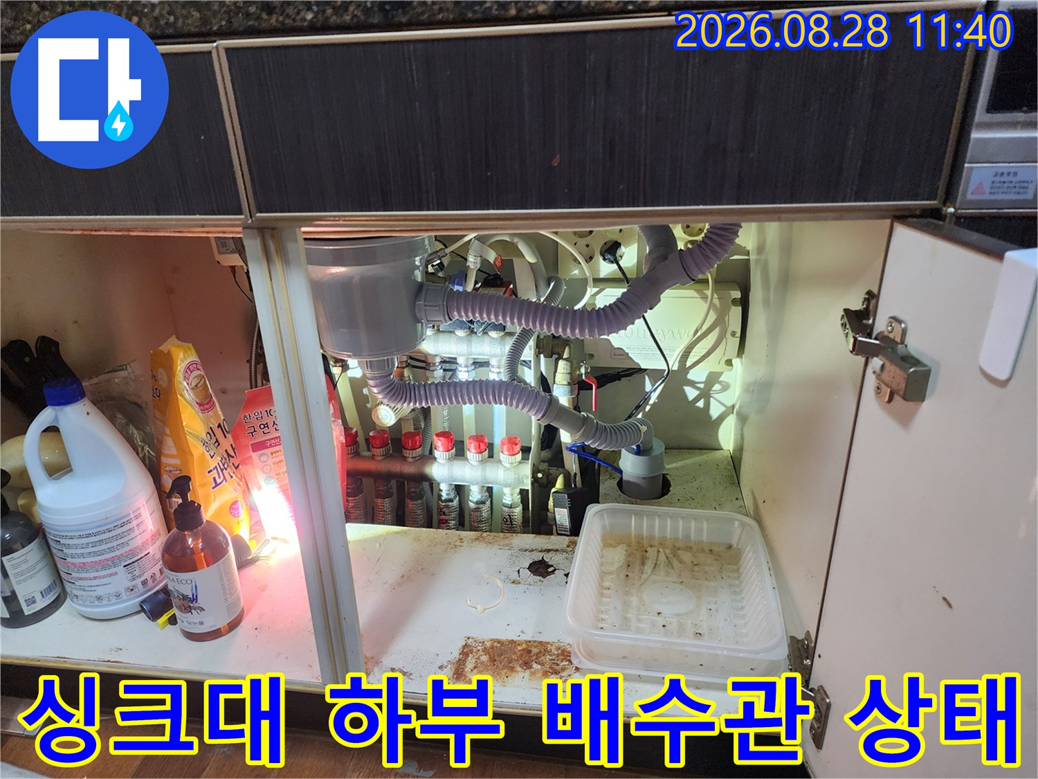 싱크대 아래쪽의 복잡한 배수 호스와 연결 부위들을 촬영한 사진입니다.