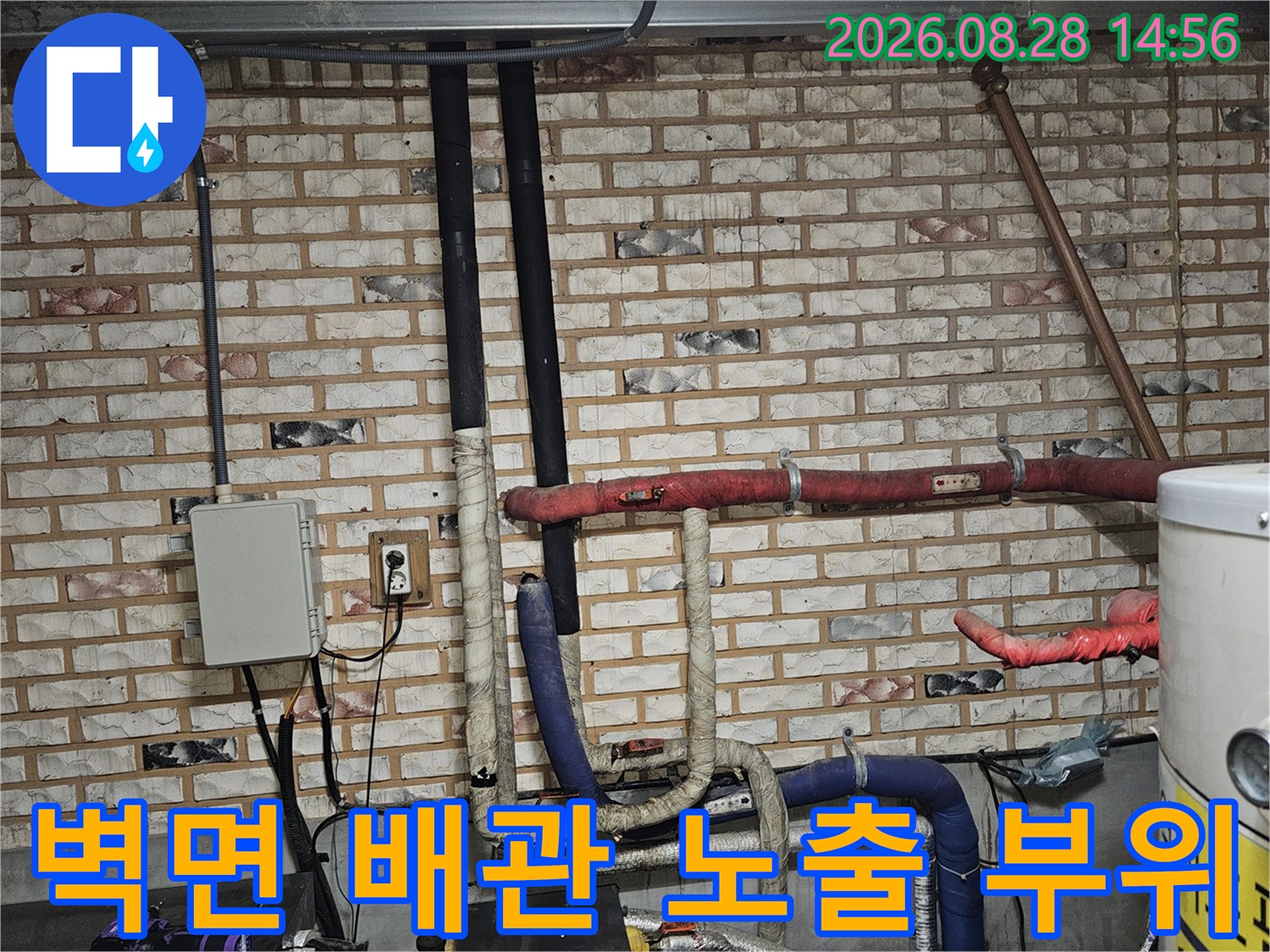 벽돌 벽면에 설치된 보온재 마감된 배관과 전기 박스 주변 모습입니다.