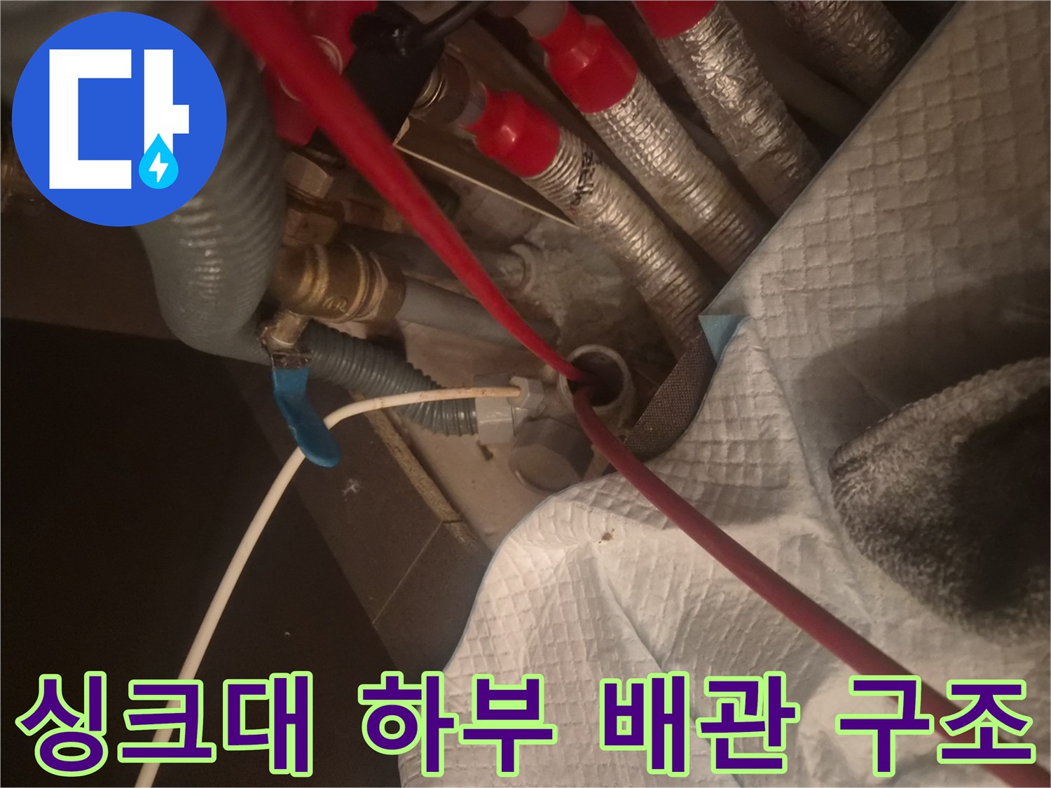 은색 보온재와 붉은색 호스가 얽혀 있는 싱크대 하단 배관 작업 현장