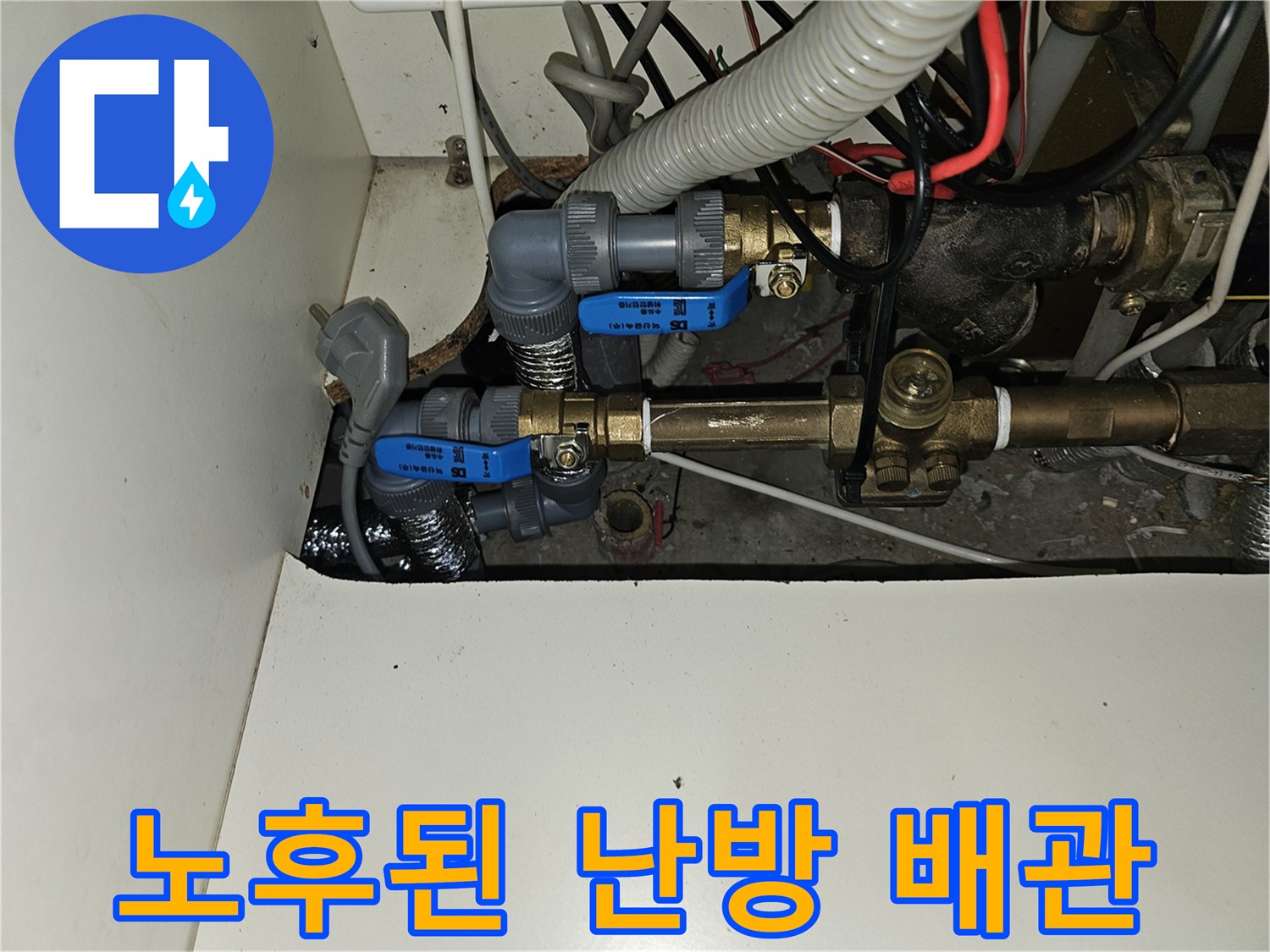 금속 배관과 파란색 밸브가 보이는 주방 하부장 내부 배관실