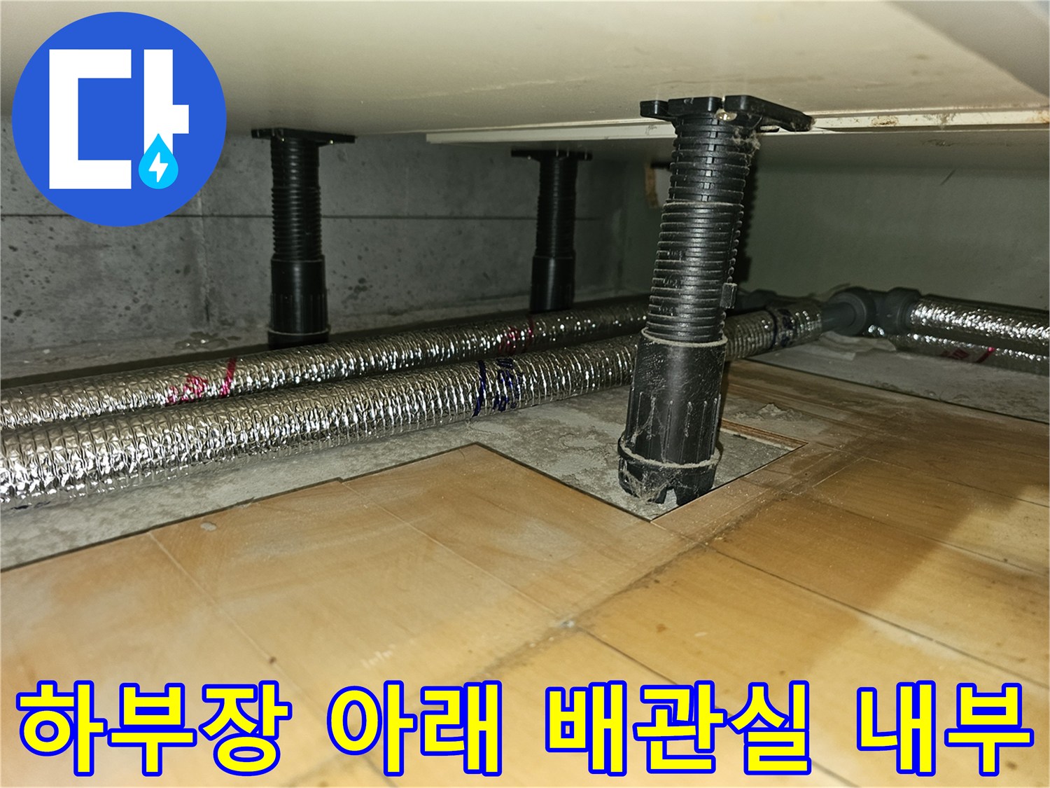 싱크대 하부장 아래 공간의 보온재 배관과 검은색 지지대 구조물