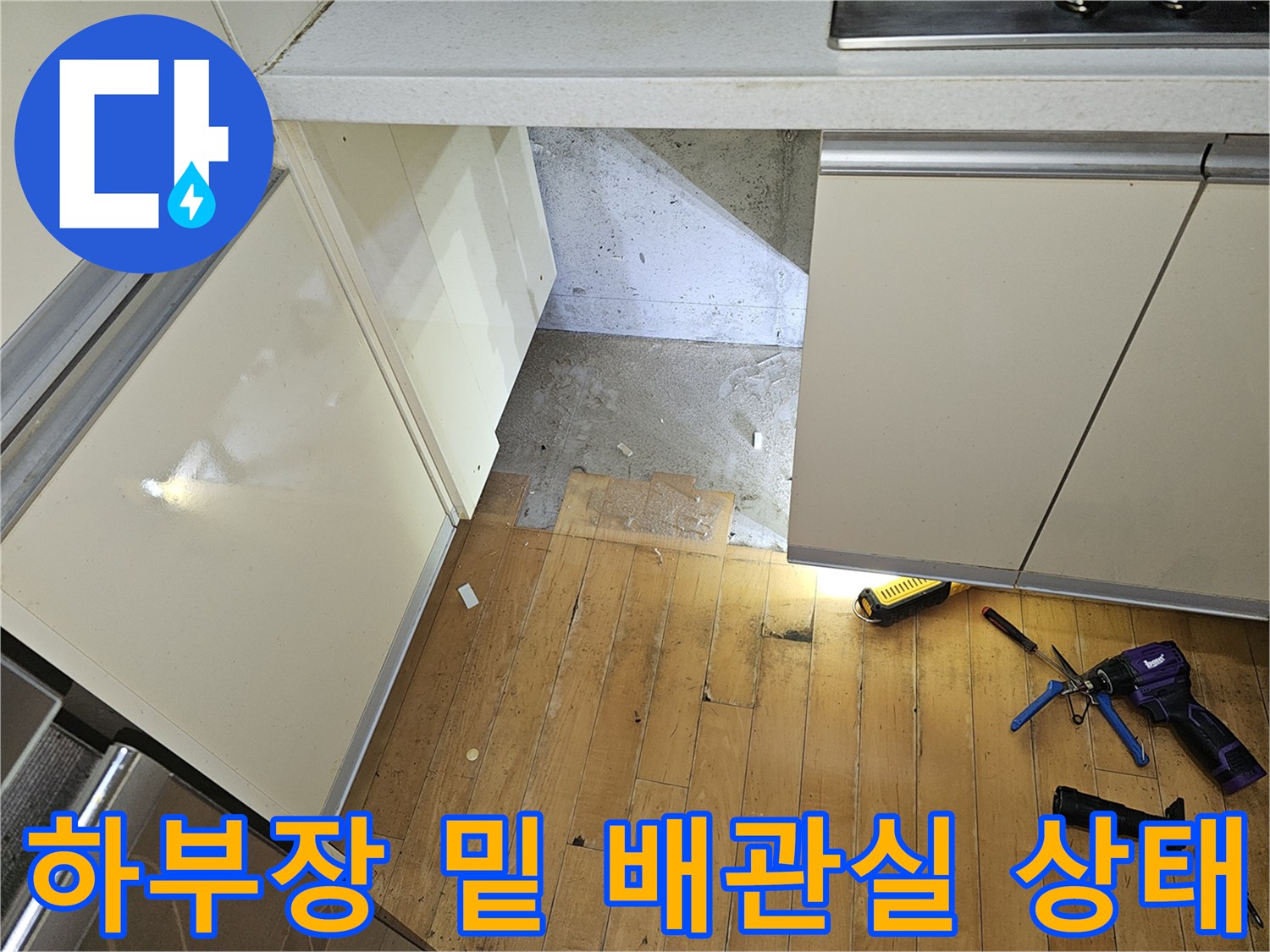 주방 싱크대 하부장 아래 뜯어진 바닥재와 작업 도구가 놓인 모습