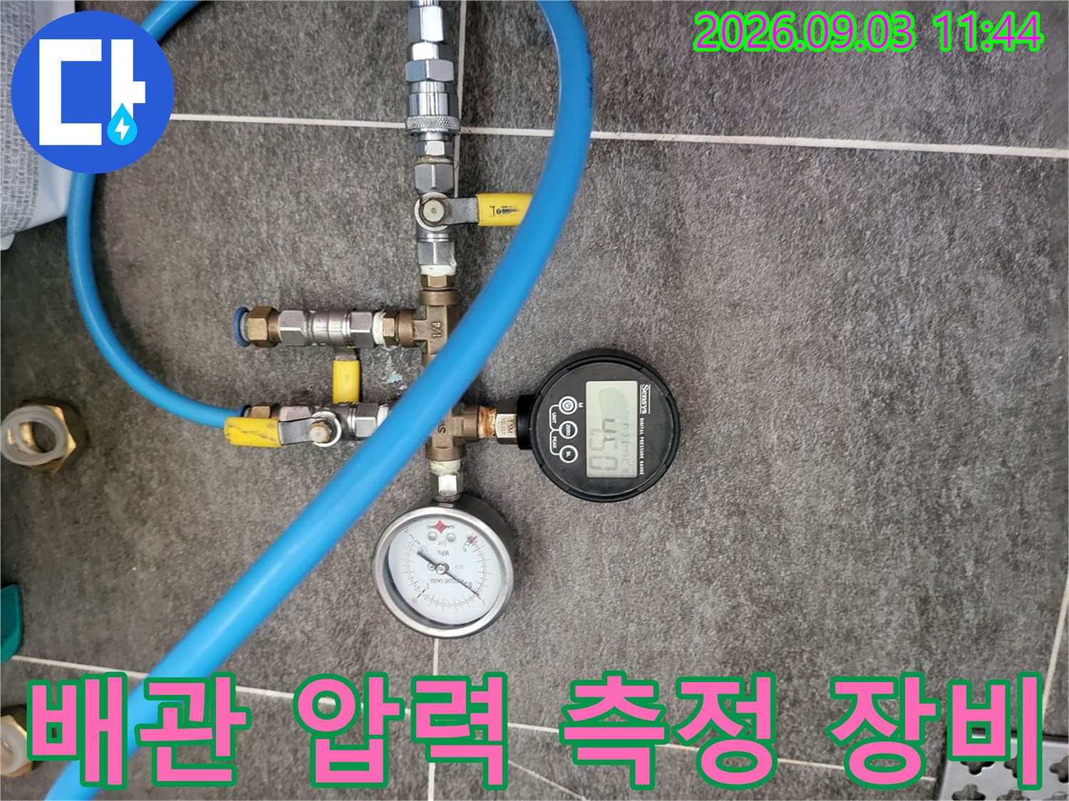 파란색 호스와 게이지가 연결된 배관 점검용 장치입니다.
