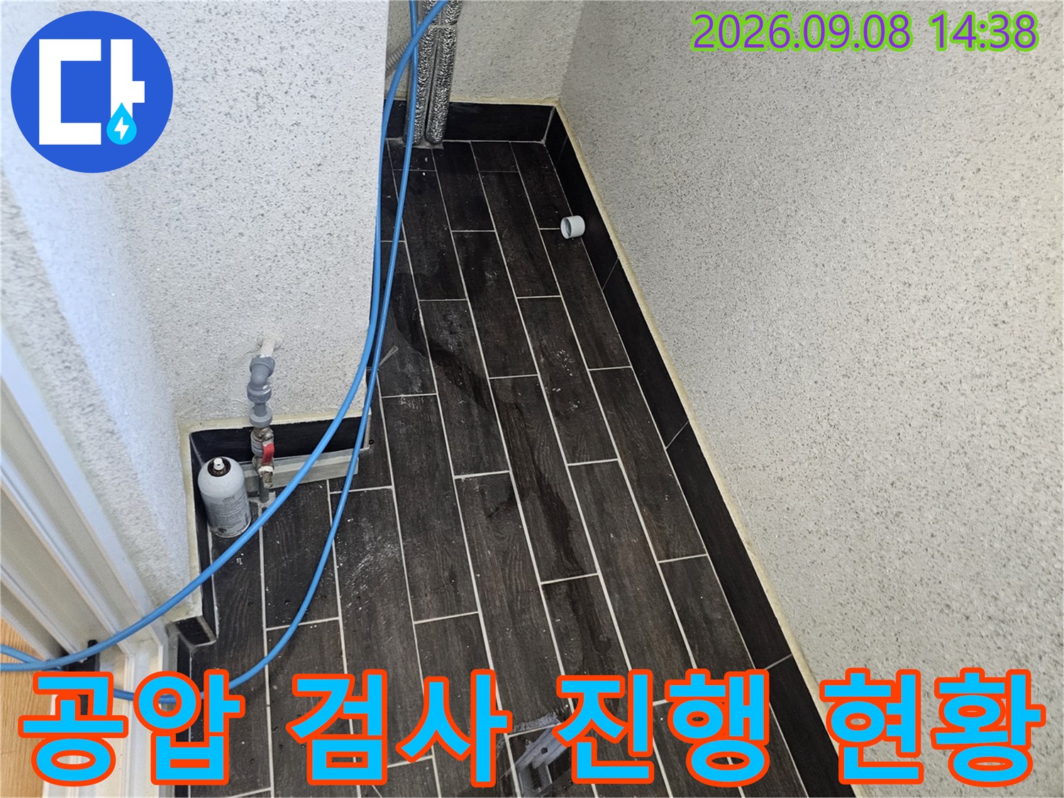 어두운 색 타일 벽면과-파란색 호스가 연결된-배관 압력 점검 모습입니다.
