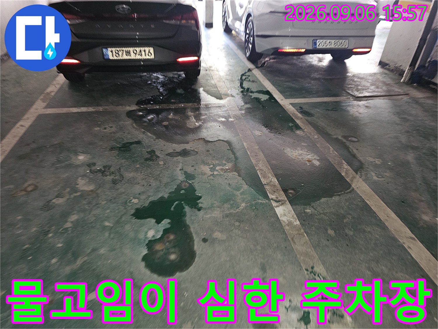 자동차 아래쪽 주차장 바닥에 물기가 번져 있는 현장 사진입니다.