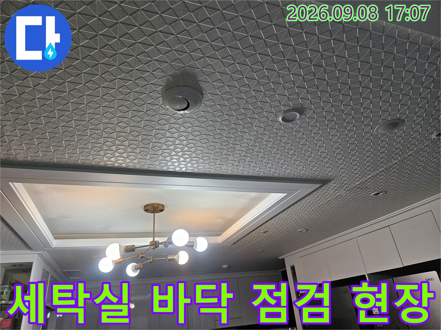 조명이 비치는 세탁실의 패턴 타일과 배수구 주변 모습입니다.
