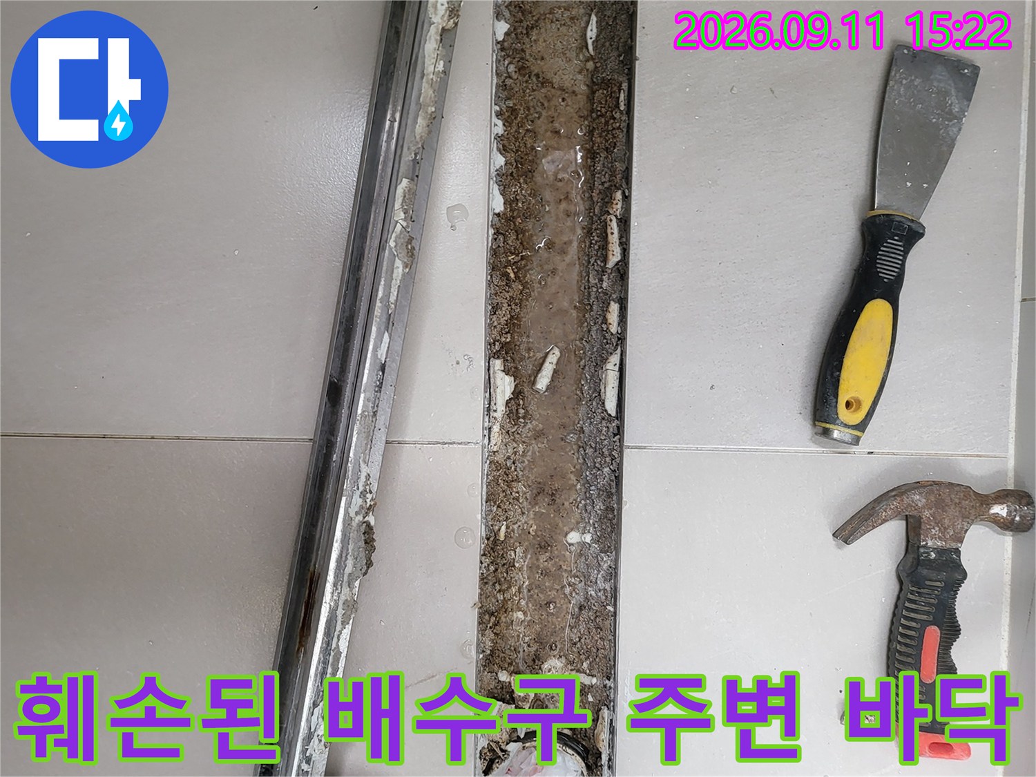 금속 배수구 덮개와 망치가 놓인 화장실 타일 철거 현장