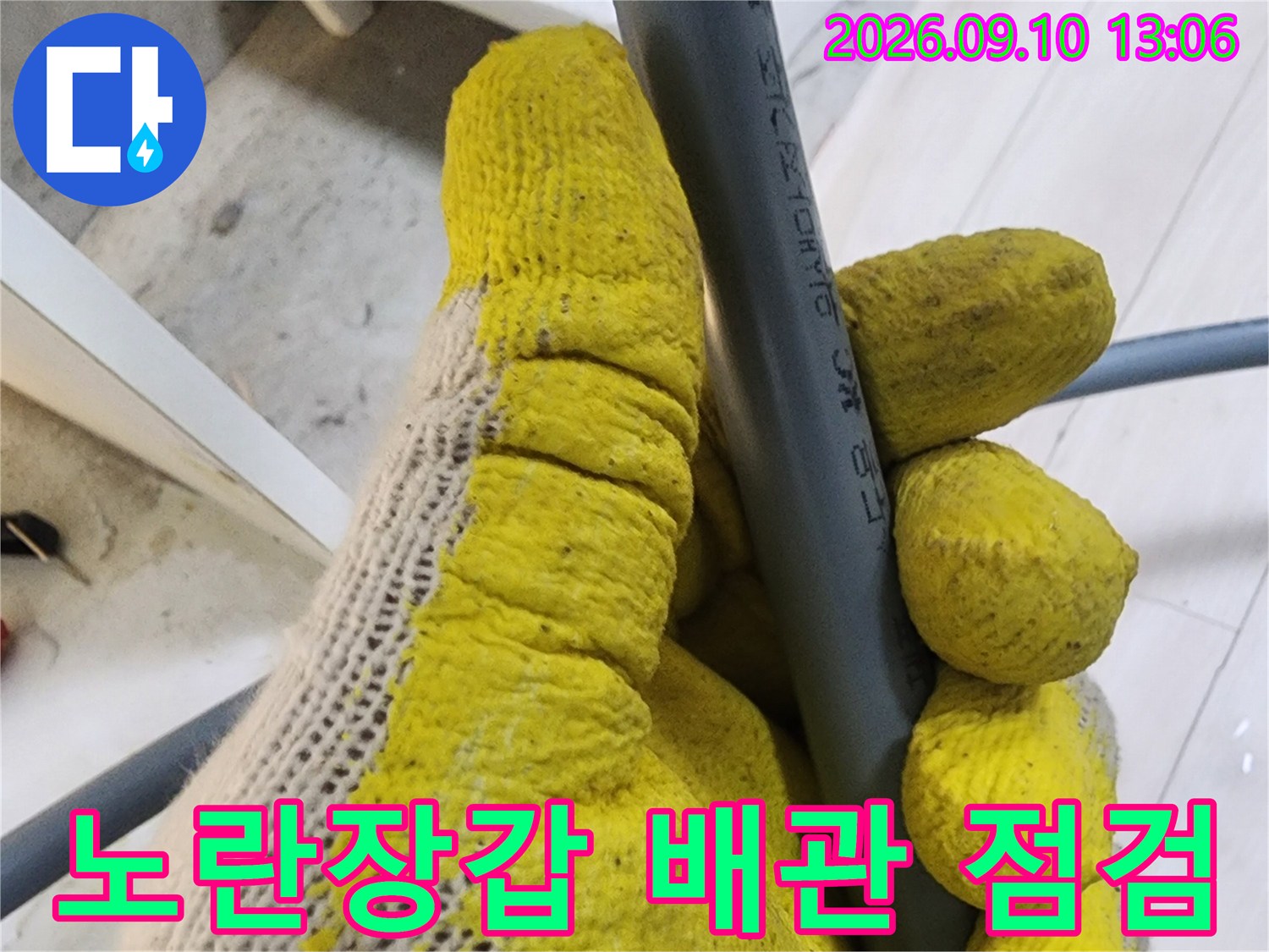 노란 작업용 장갑이 회색 수도 배관을 잡고 있는 모습
