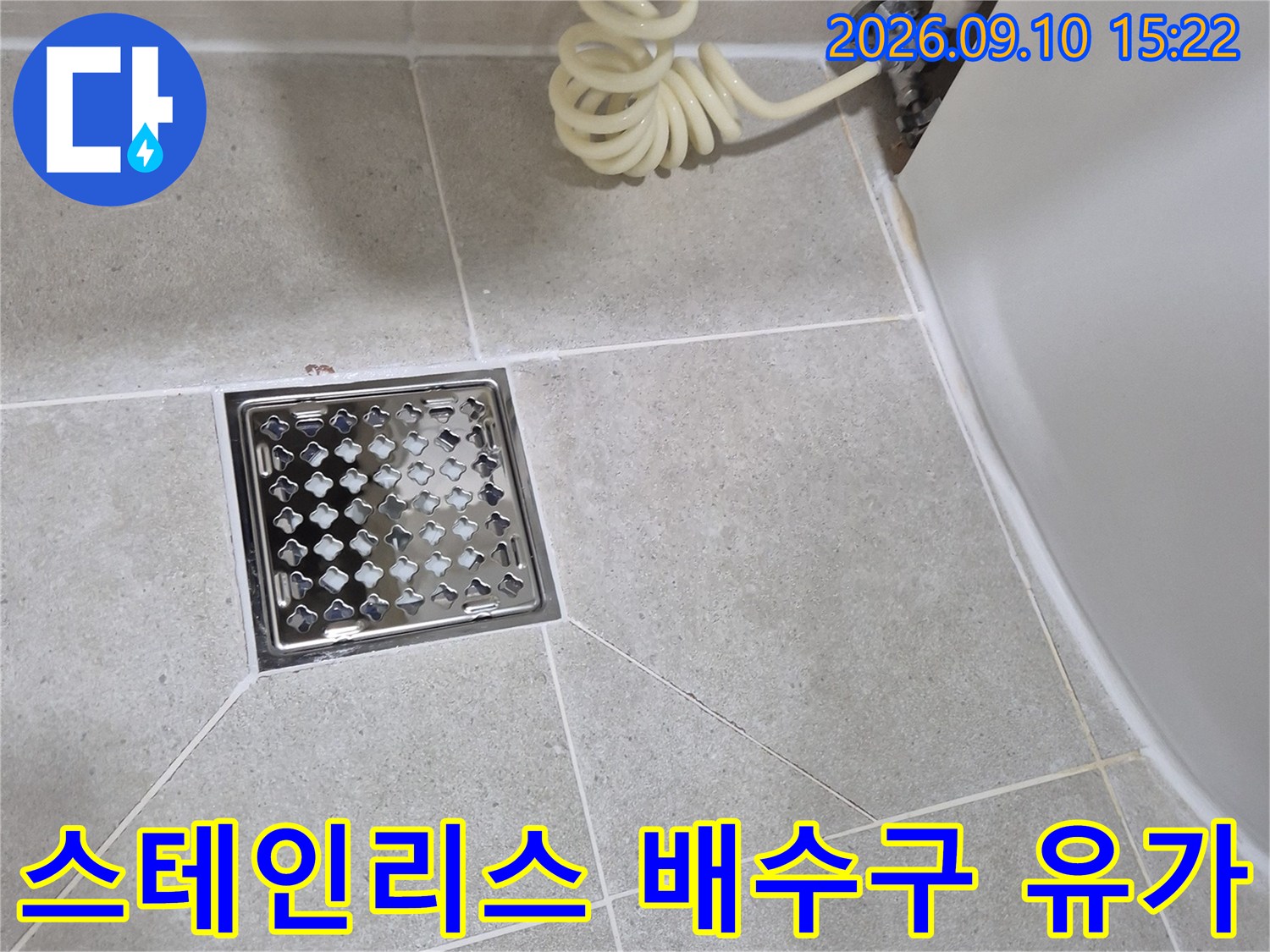 밝은 톤의 욕실 타일과 금속 재질 배수구 입구 모습