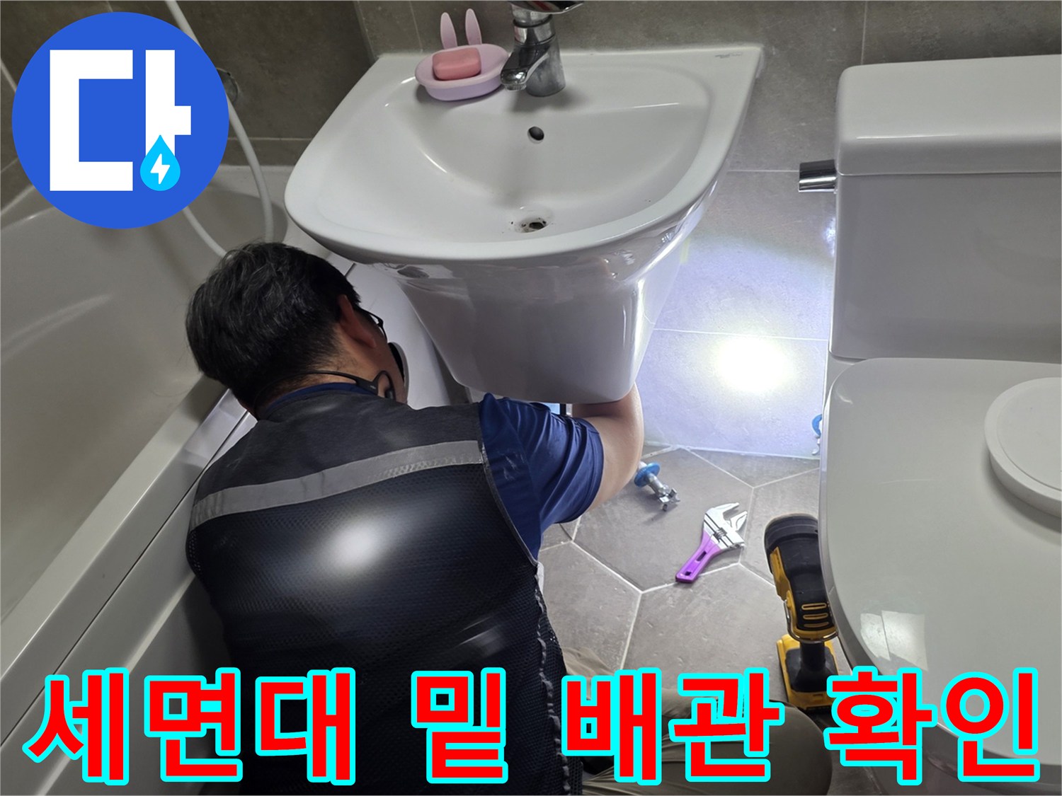 공구를 사용하여 세면대 하단 배관의 누수 여부를 조사합니다.