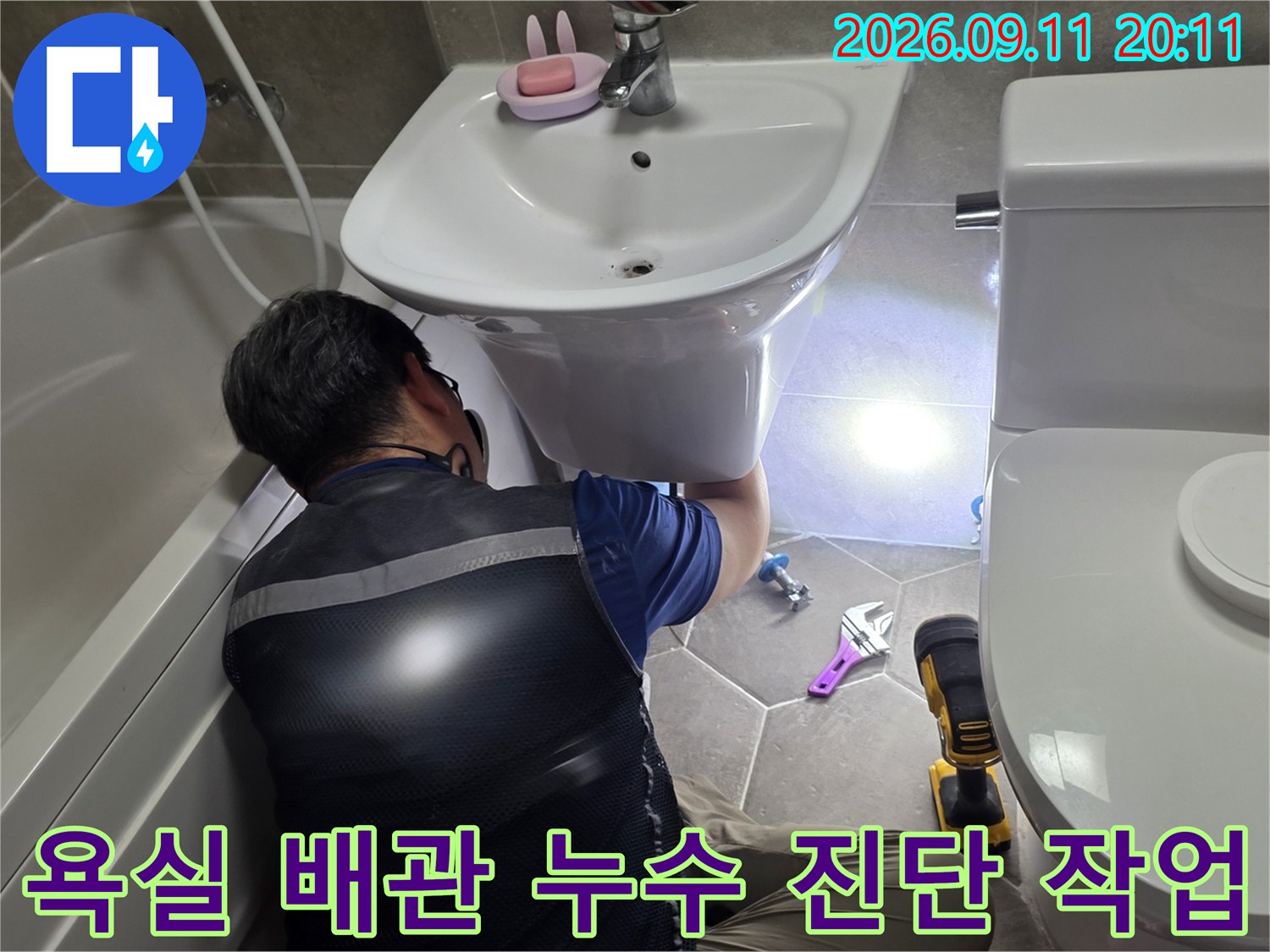 스패너와 도구를 사용하여 세면대 하부의 배관 연결부를 정밀하게 점검합니다.