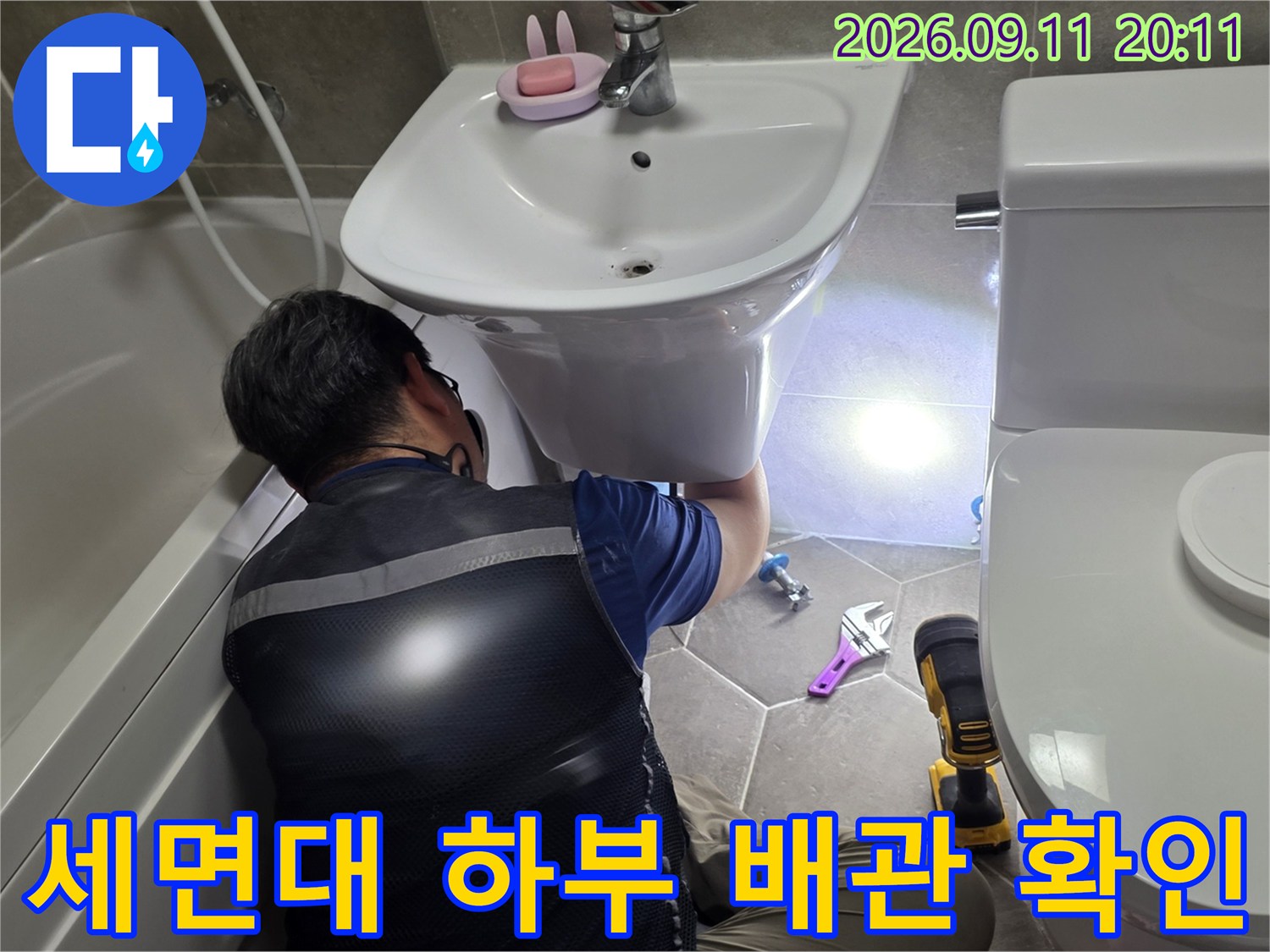 작업자가 세면대 아래쪽의 누수 지점을 찾기 위해 공구를 사용하는 모습입니다.