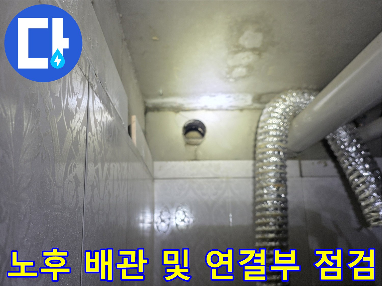 천장 배관-벽면 타일과 연결된 은색 보온재 배관의 근접 촬영본입니다.